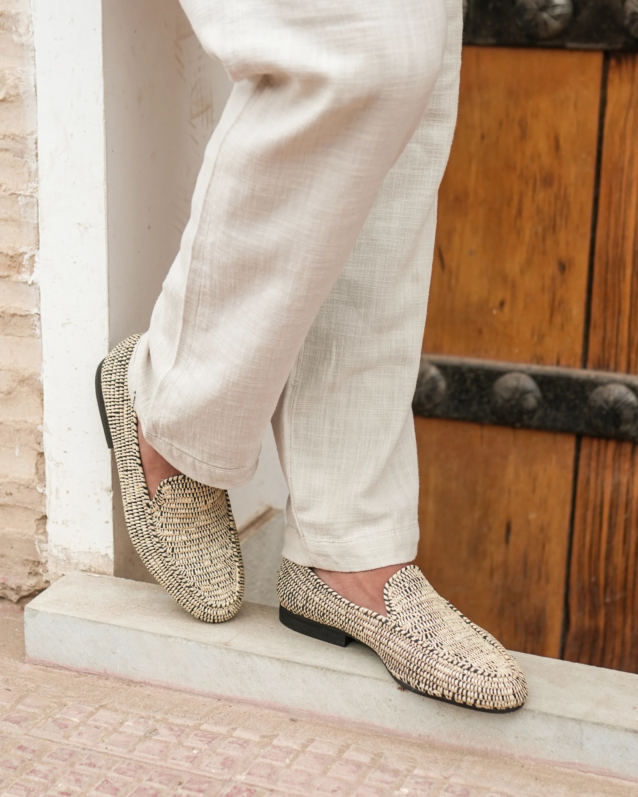 Person wearing beige woven loafers and light-colored pants on a stone step.