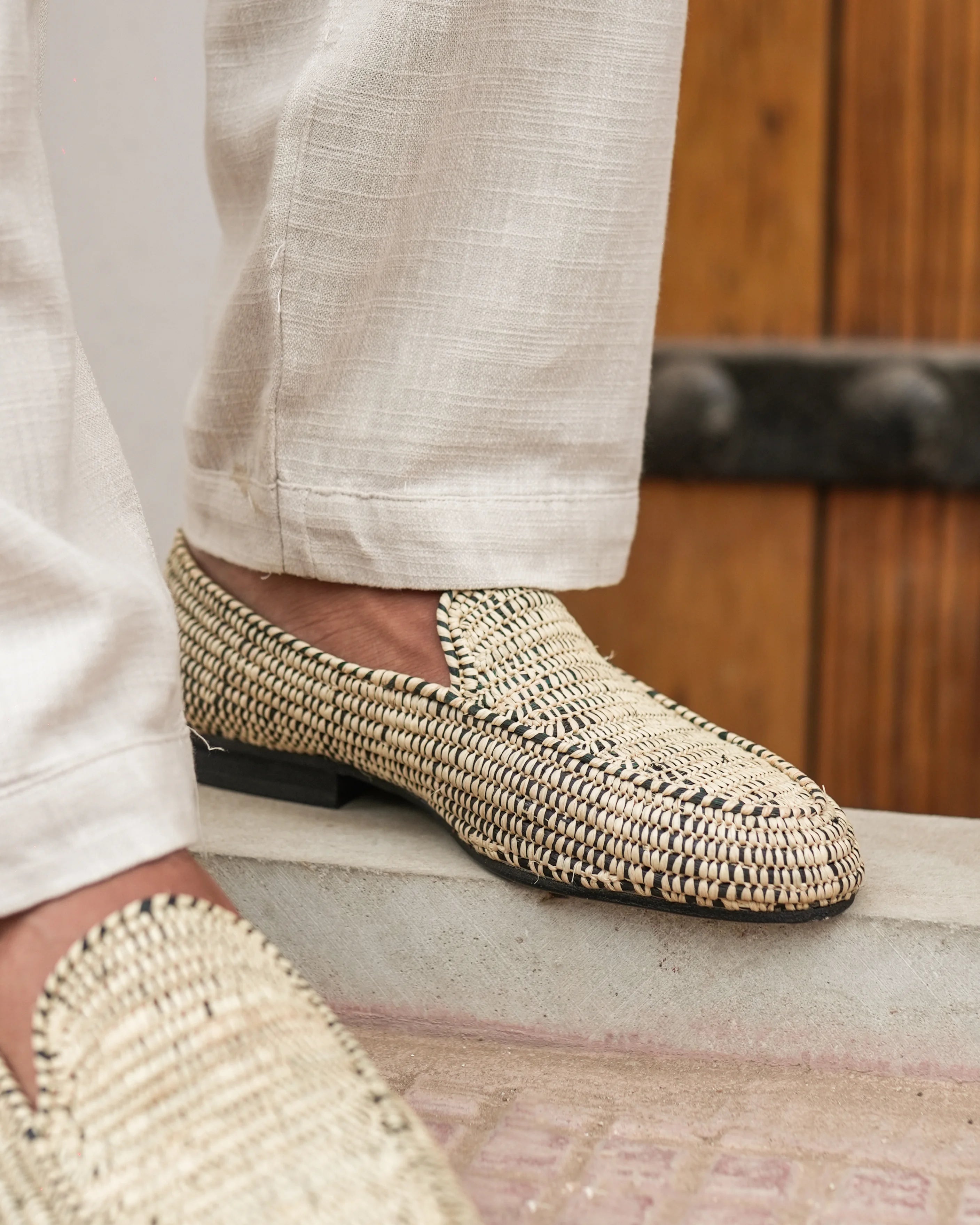 Woven shoes worn with light-colored pants on a wooden floor.