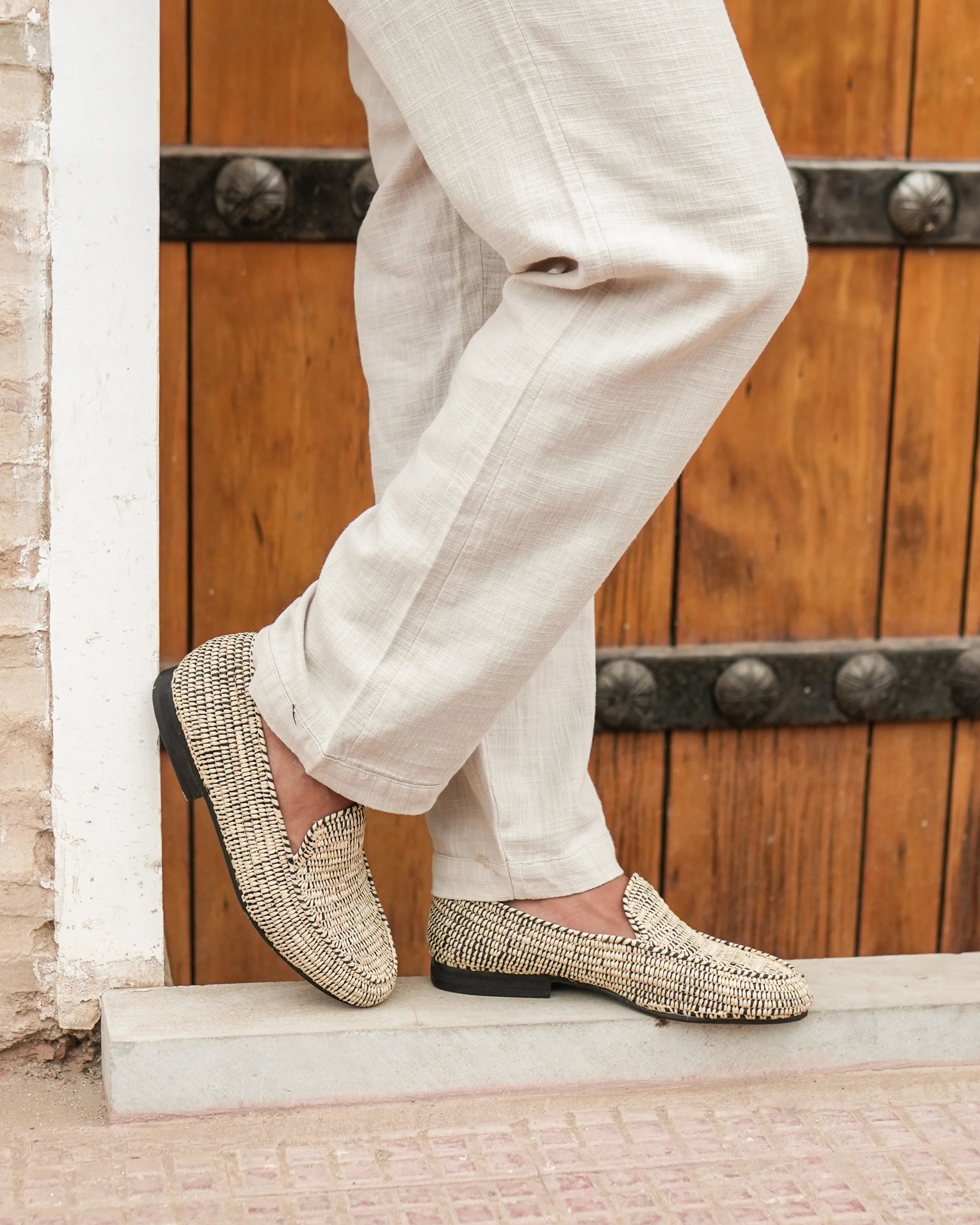 Person wearing beige loafers and light-colored pants standing on a step with a wooden door in the background.