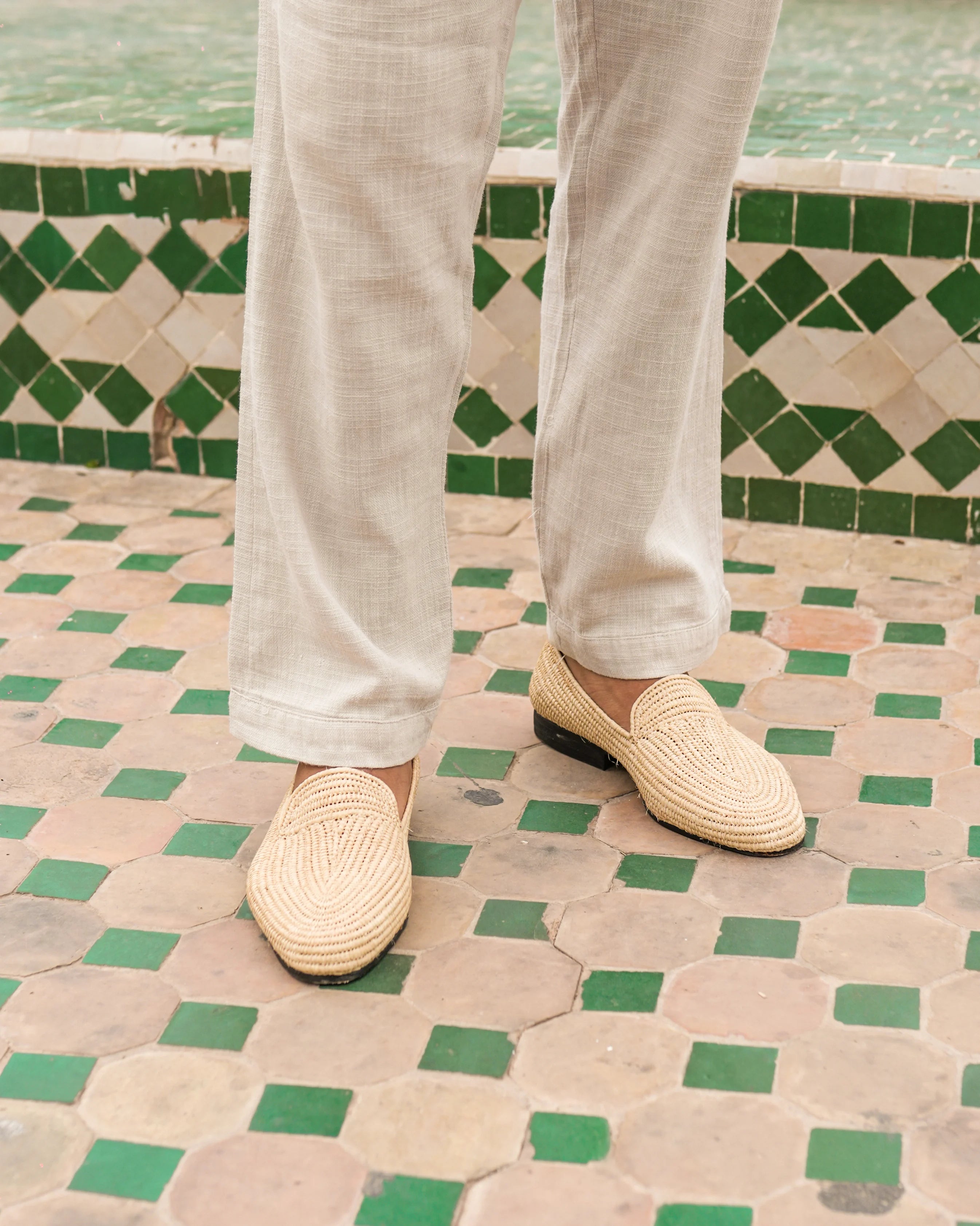 Person wearing light-colored pants and woven shoes on a patterned floor.