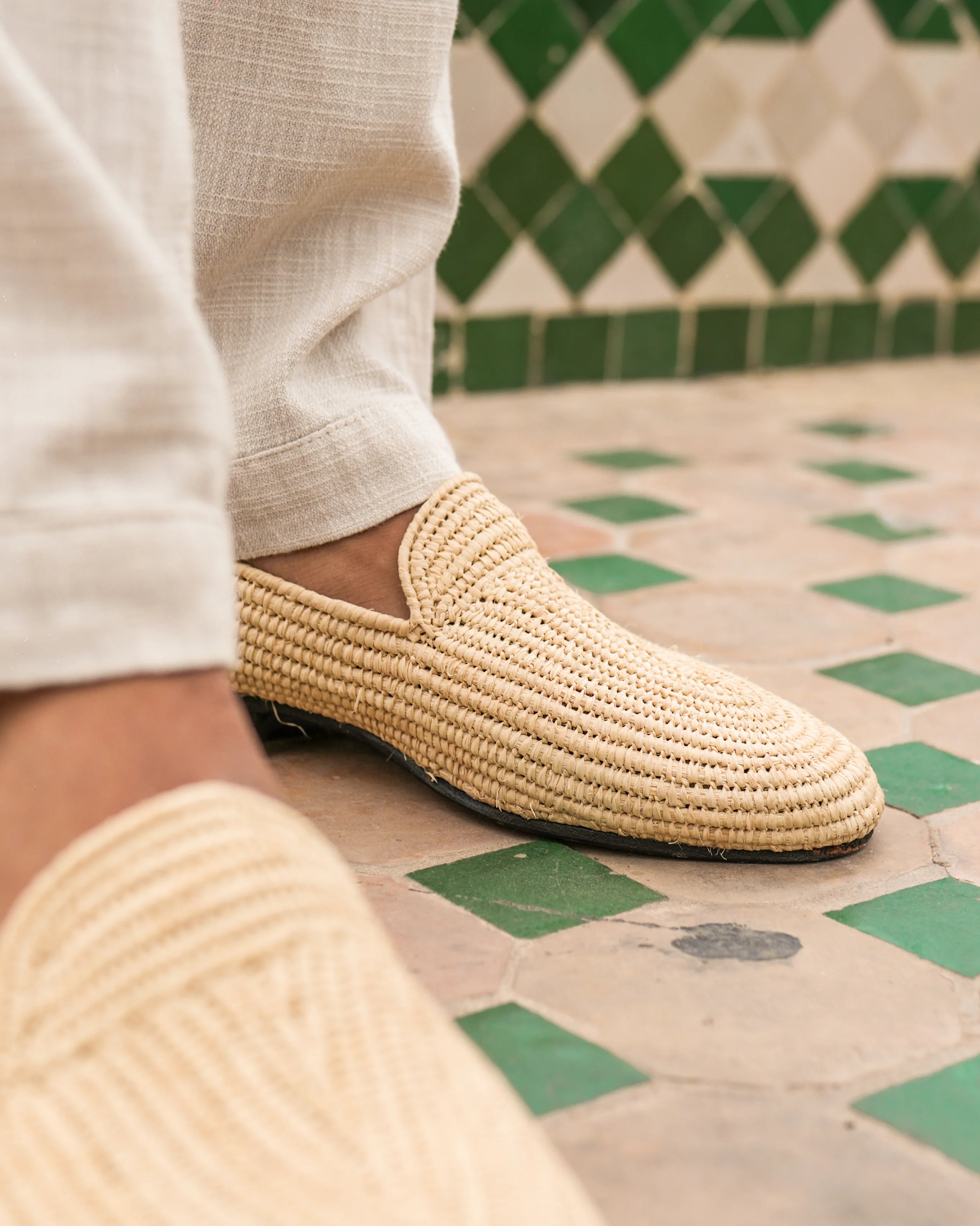 Woven shoe worn on a checkered floor with green tiles