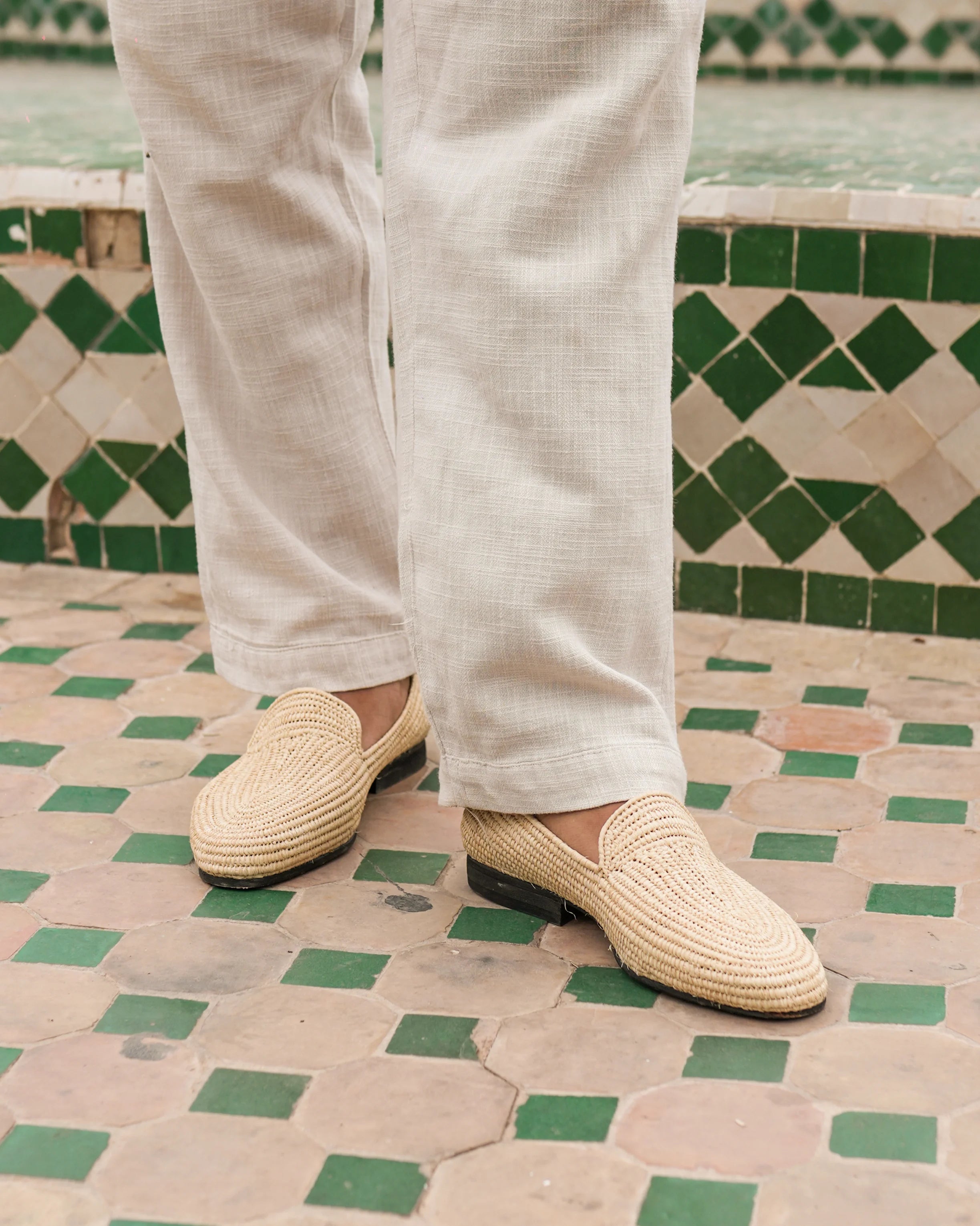 Person wearing beige woven shoes on a patterned floor with green and beige tiles.