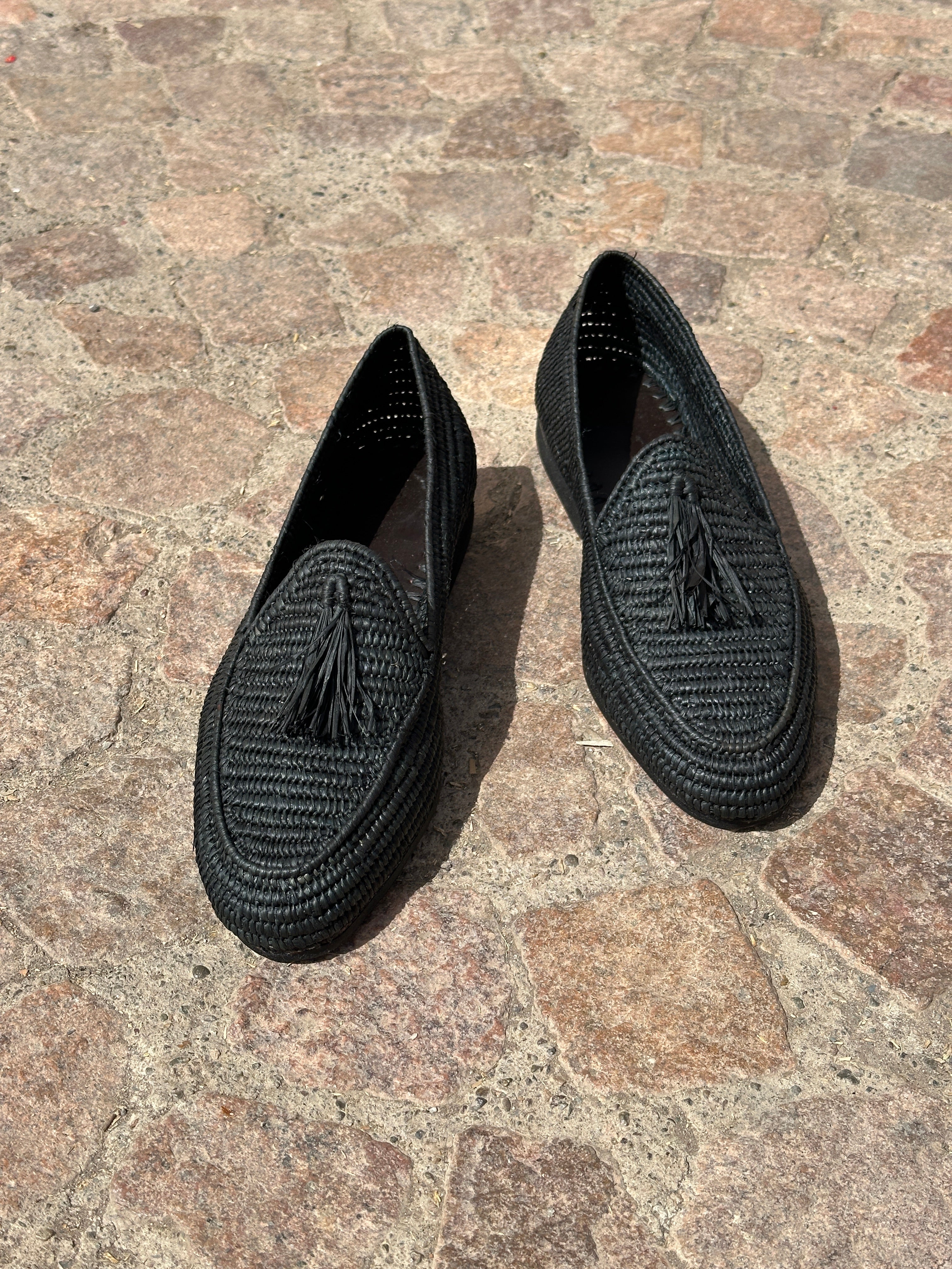 Pair of black raffia slippers on a stone surface