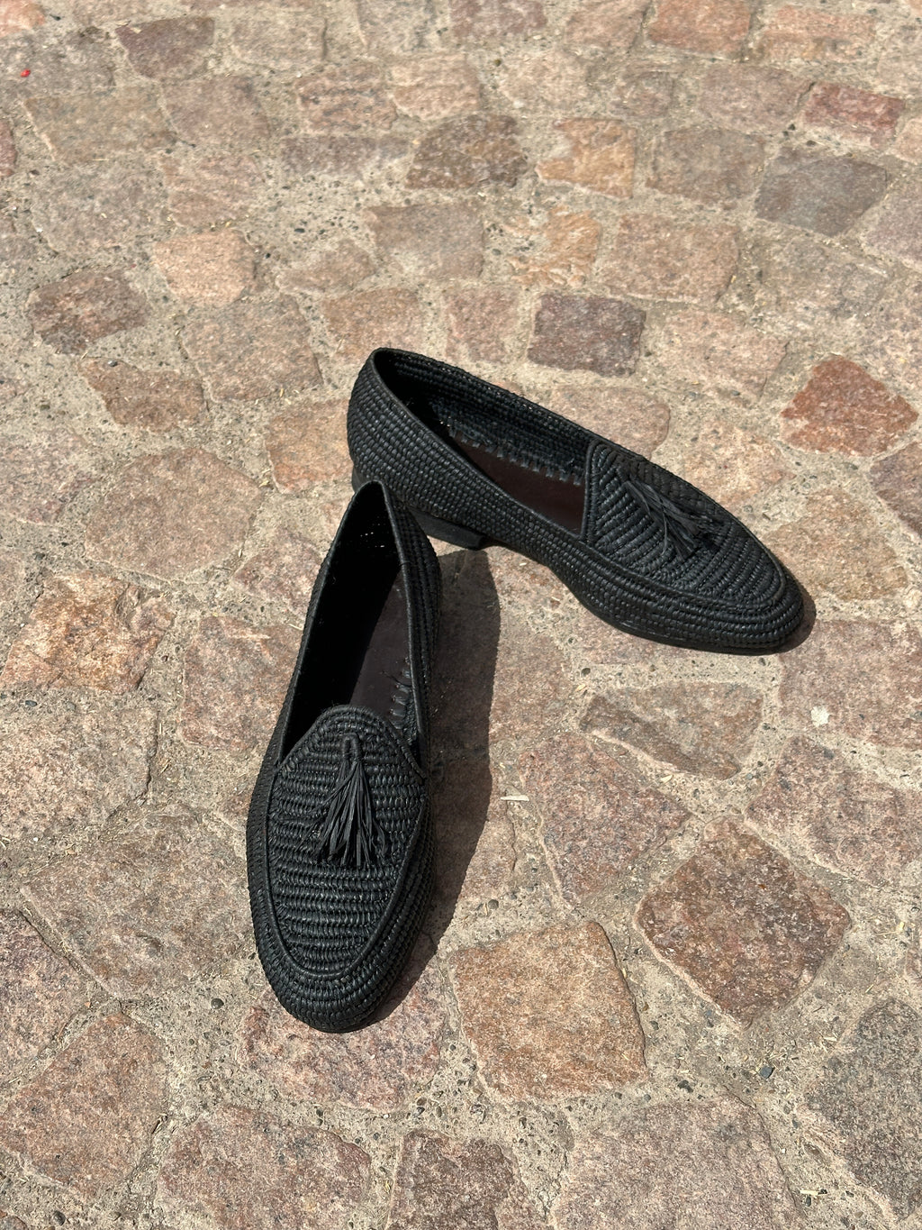 Pair of black raffia loafers on a stone pavement