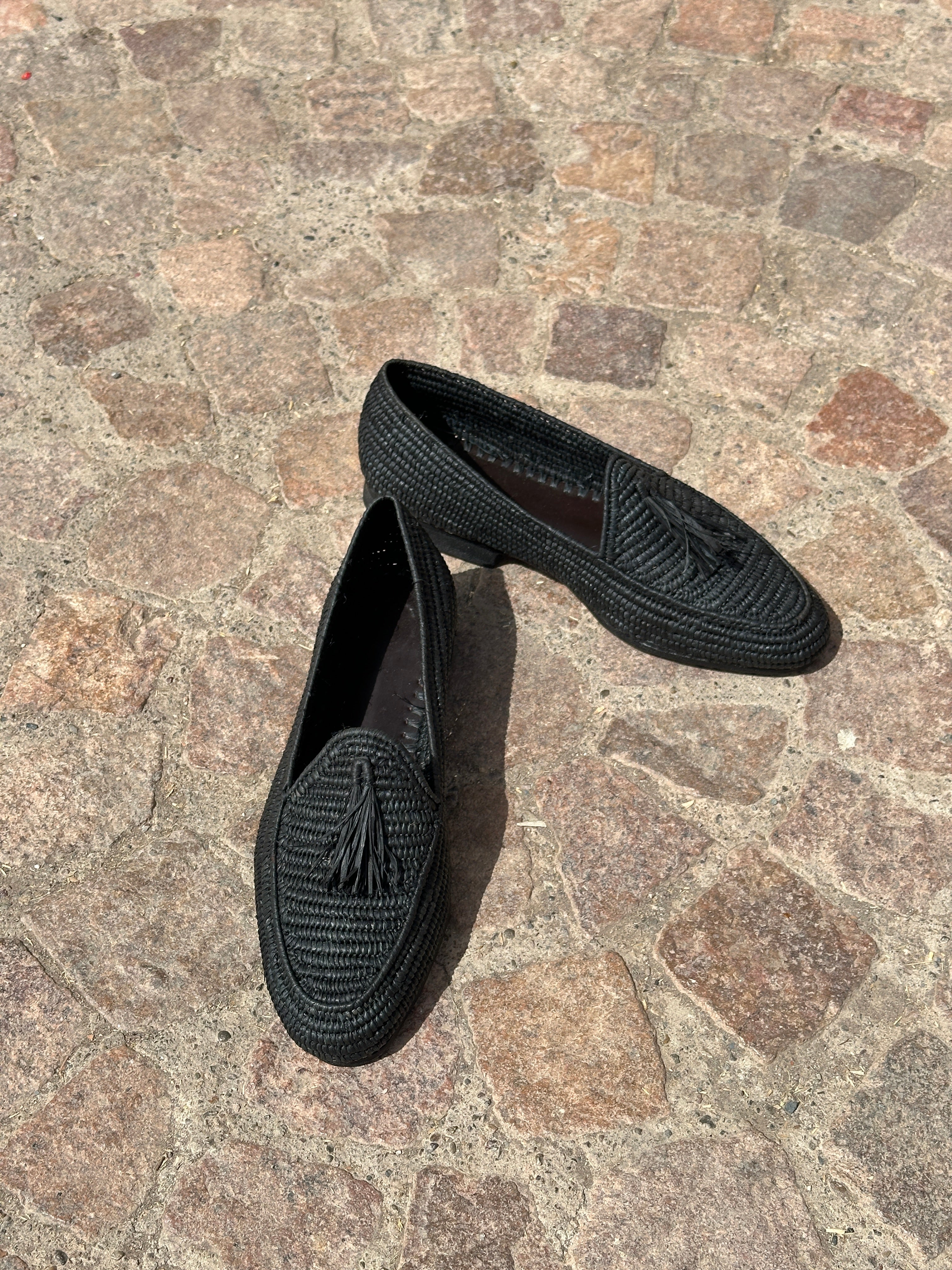 Pair of black raffia loafers on a stone pavement