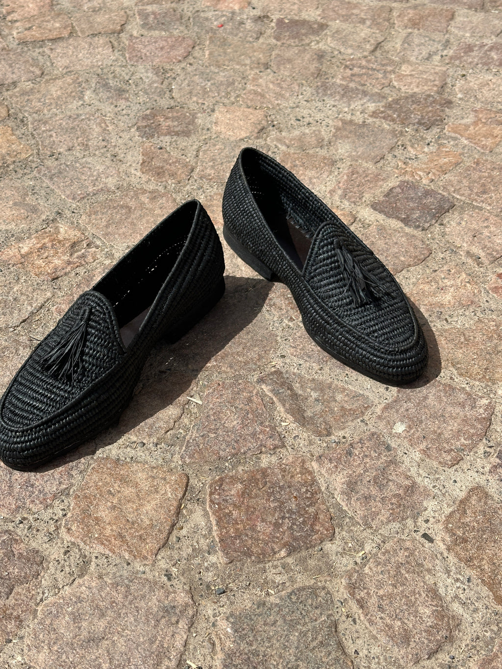 Black woven raffia shoes on a stone pavement