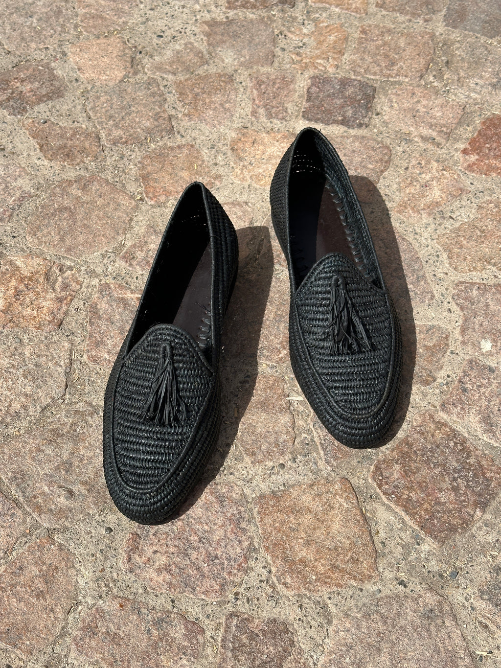 Pair of black raffia loafers on a stone pavement
