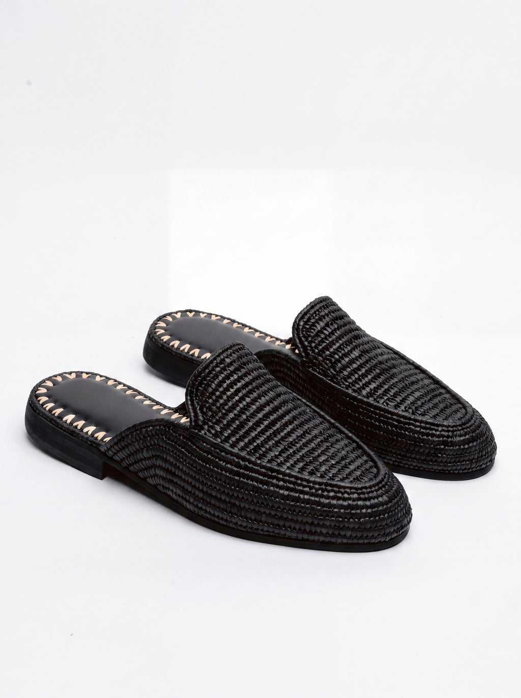 A pair of black woven slip-on mule loafers with gold-tone decorative stitching along the edge of the sole, displayed on a clean white background.