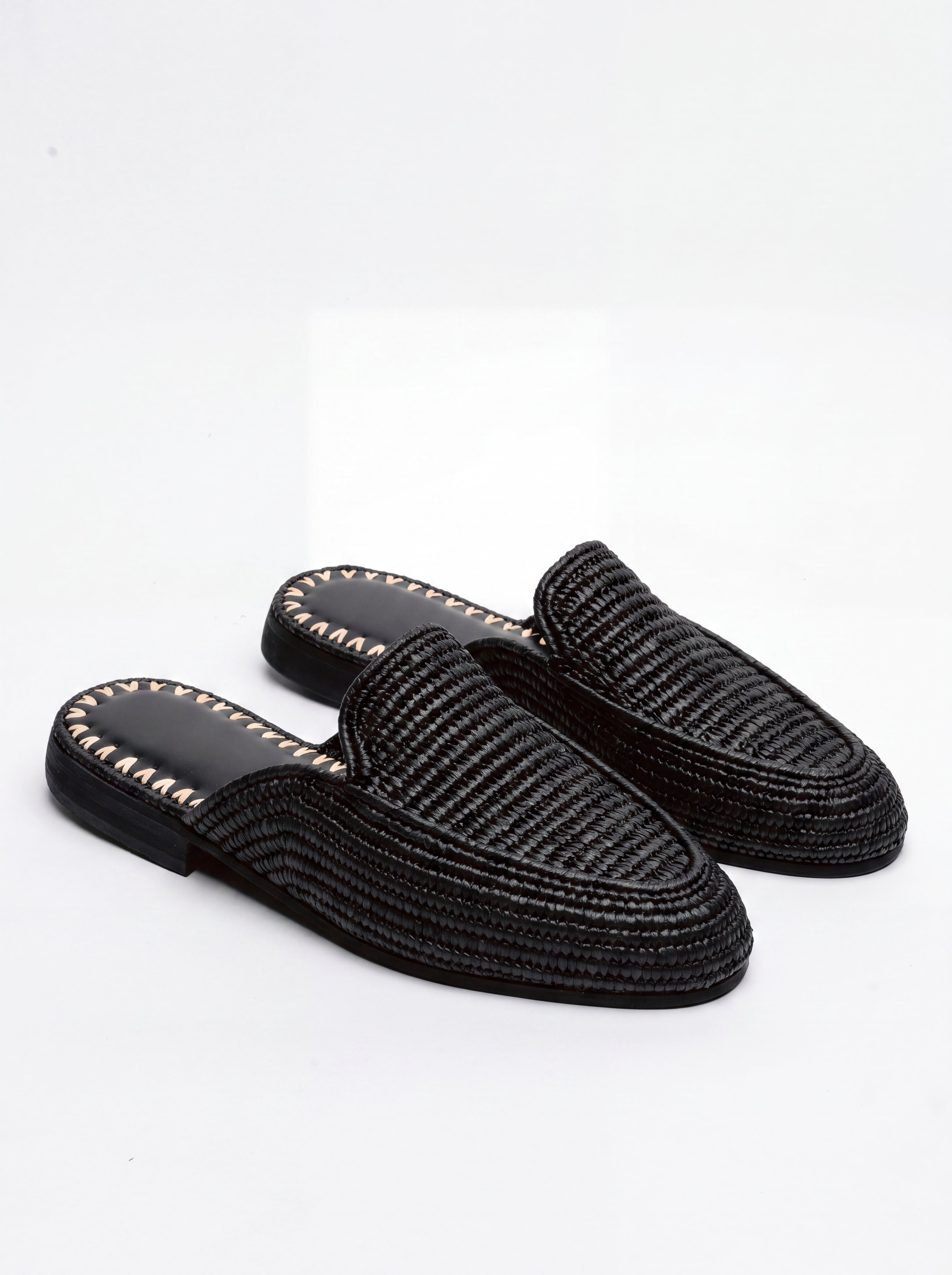 A pair of black woven slip-on mule loafers with gold-tone decorative stitching along the edge of the sole, displayed on a clean white background.