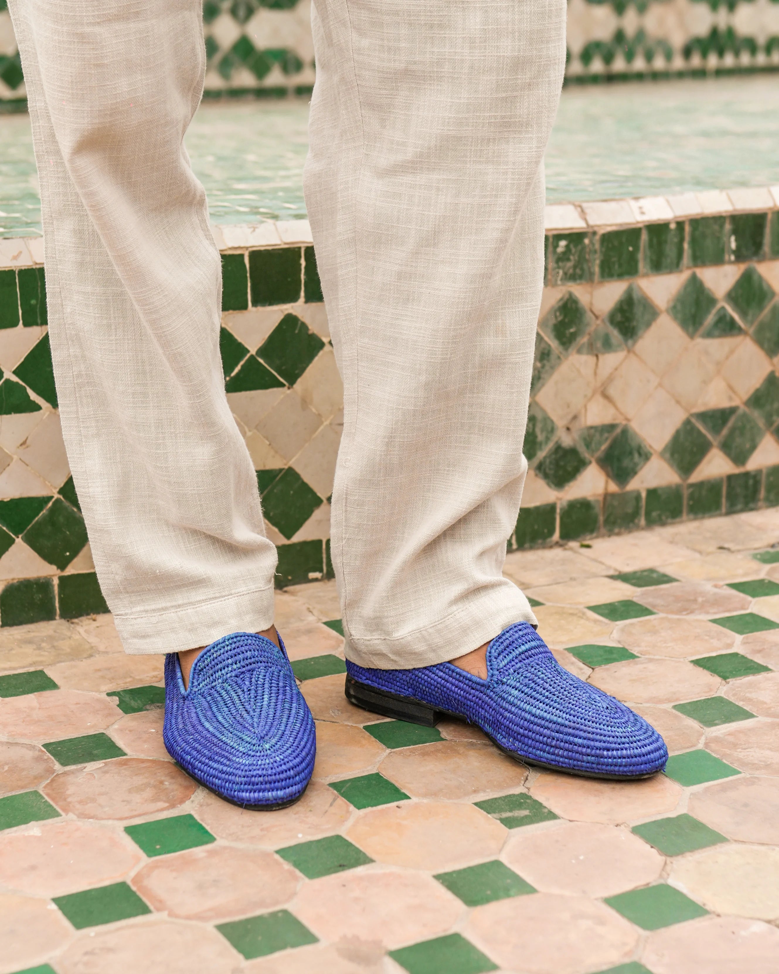 Blue woven shoes worn with light-colored pants on a patterned floor.