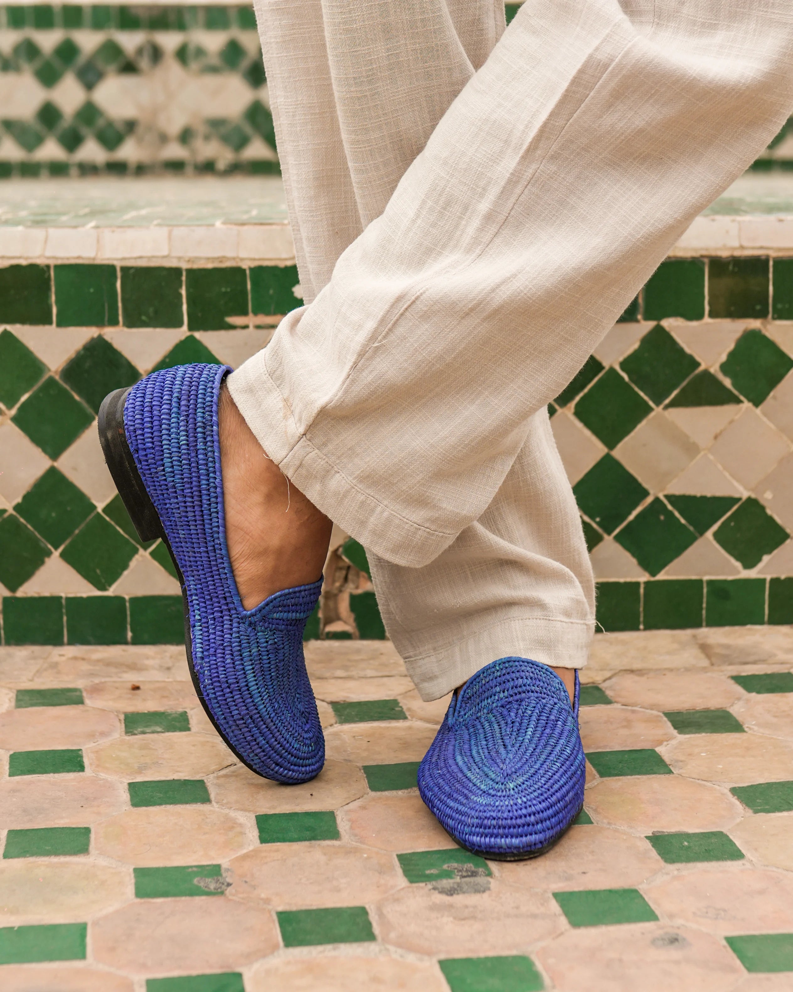 Blue woven shoes worn with beige pants on a patterned floor.