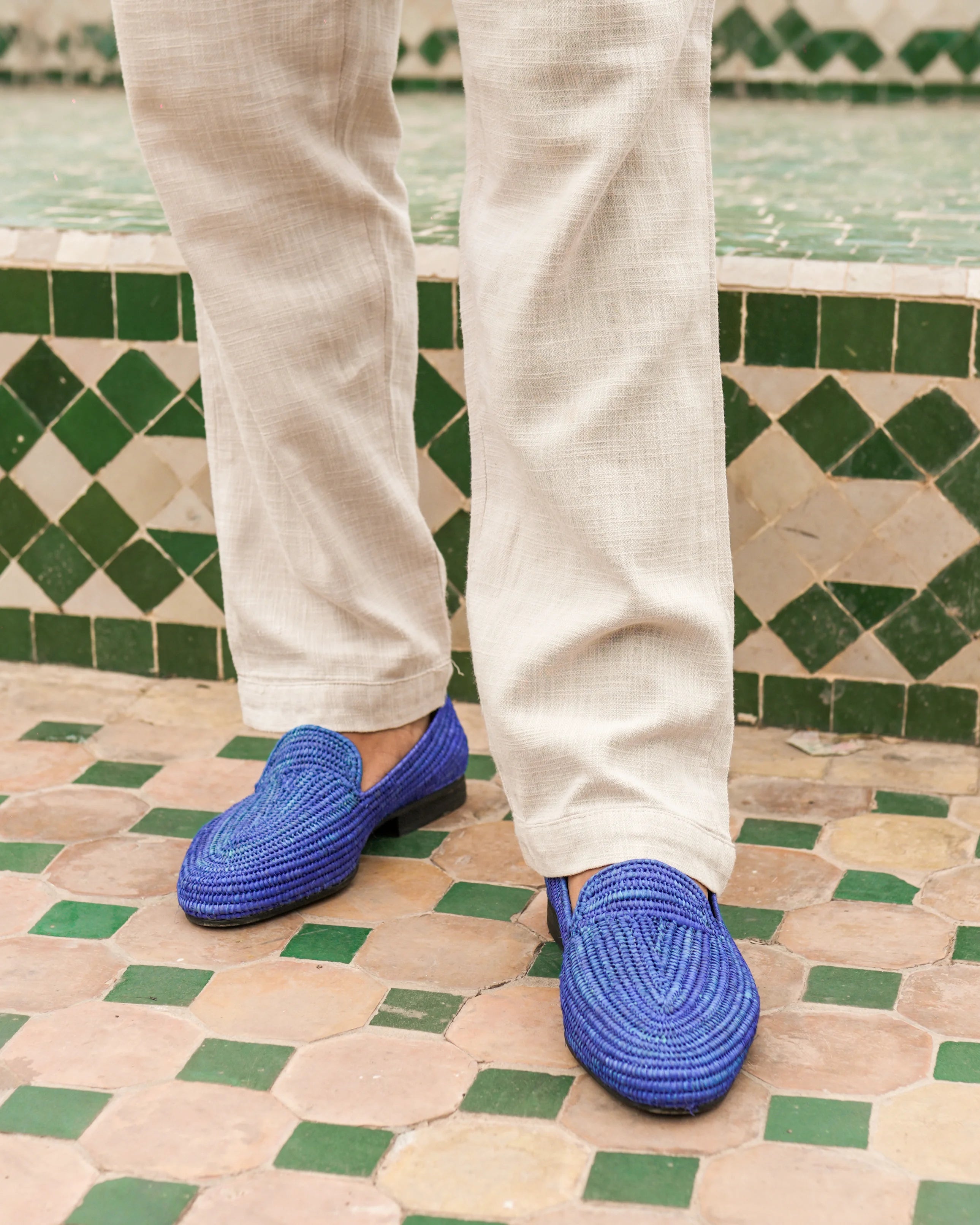 Blue woven shoes worn with white pants on a patterned floor.