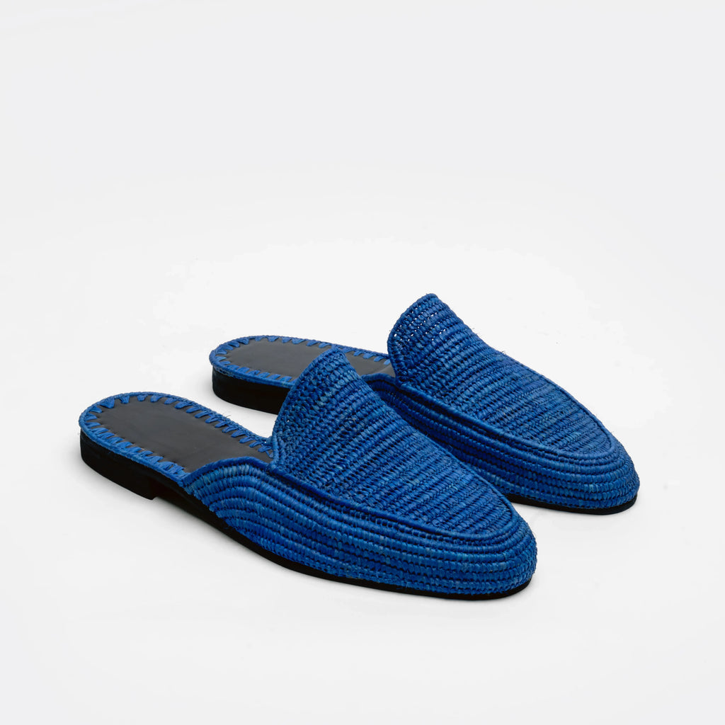 A pair of blue woven slip-on mule with black soles, displayed on a clean white background.