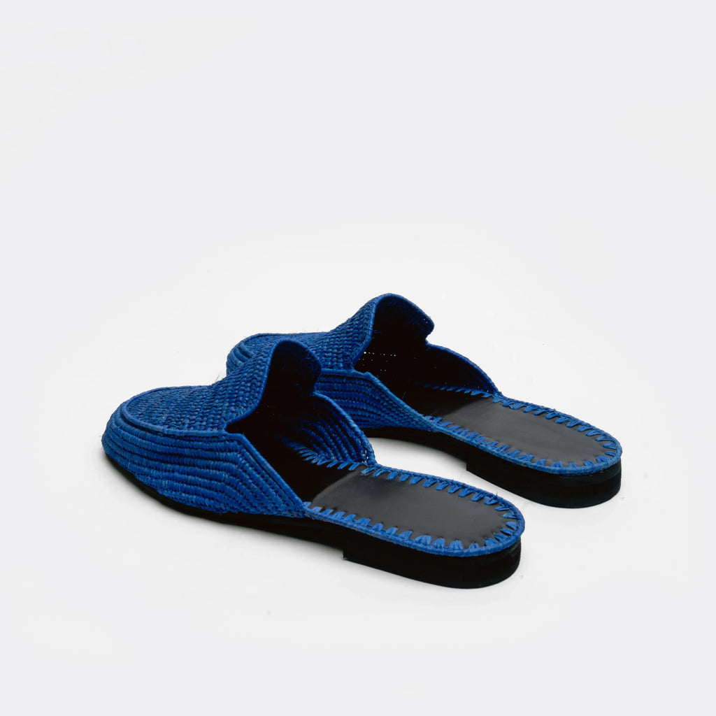 A pair of blue woven mule sandals with black soles, photographed on a clean white background.