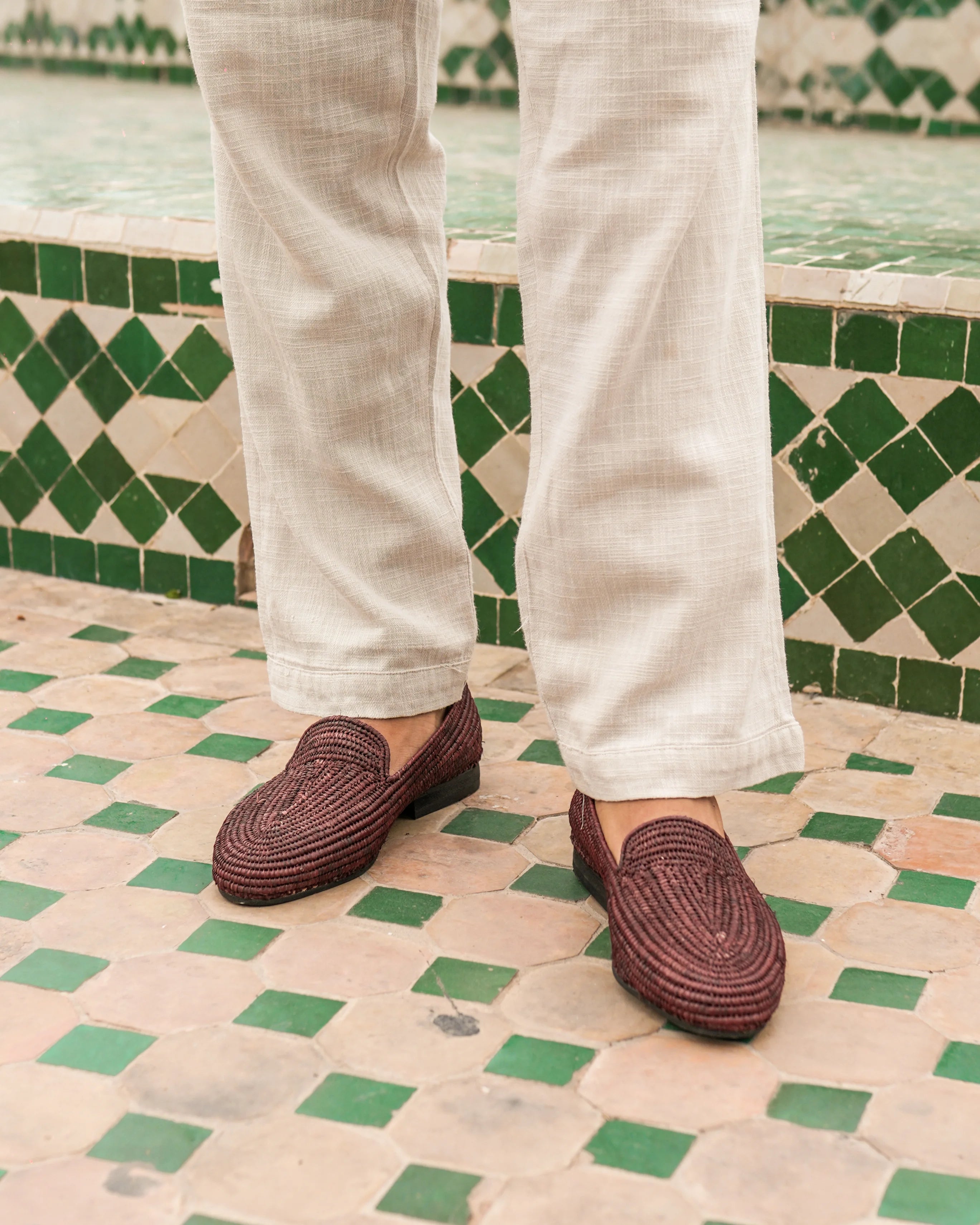 Brown loafers worn with white pants on a patterned floor.
