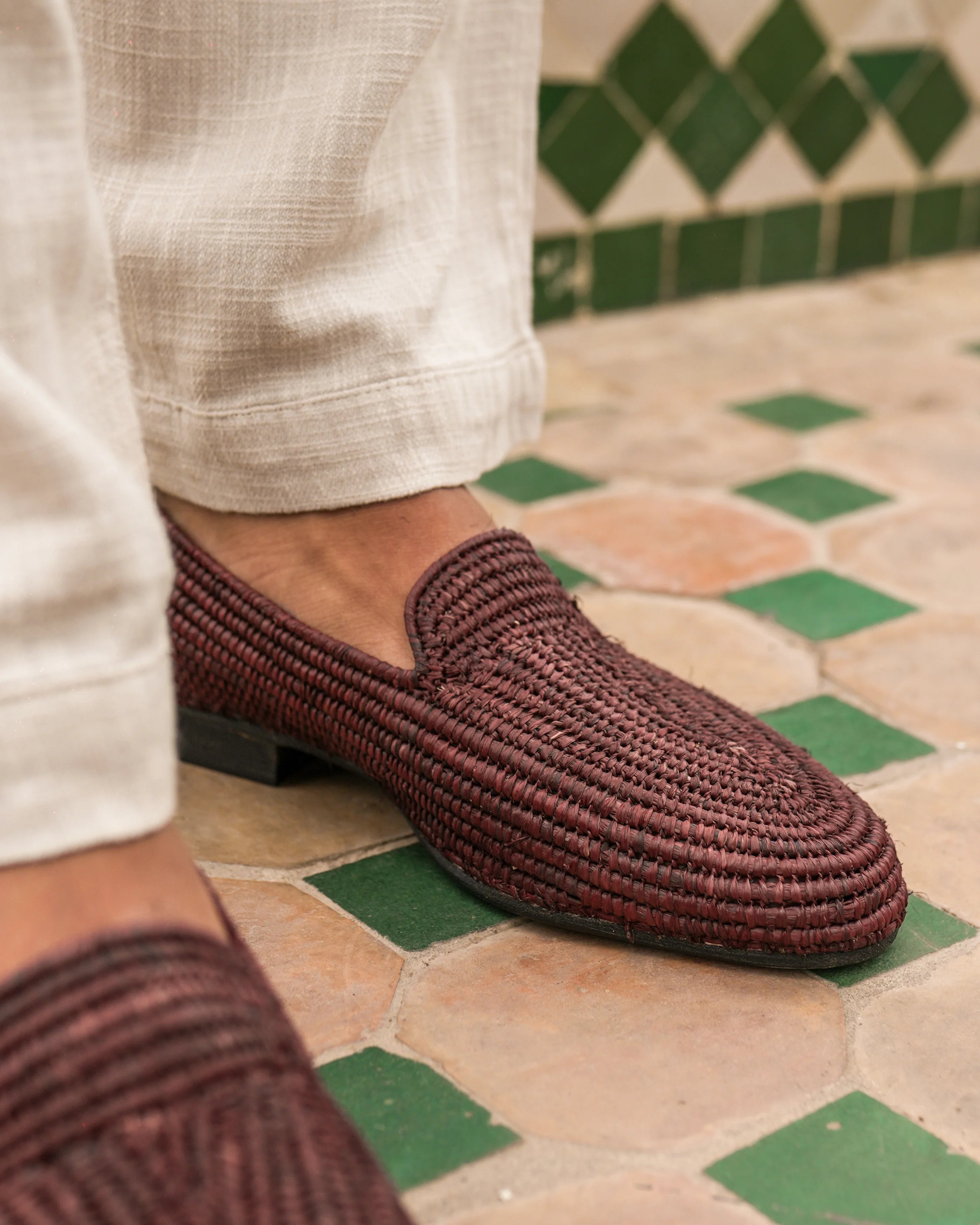 Brown woven loafer on a foot with tiled floor and green tiles in the background