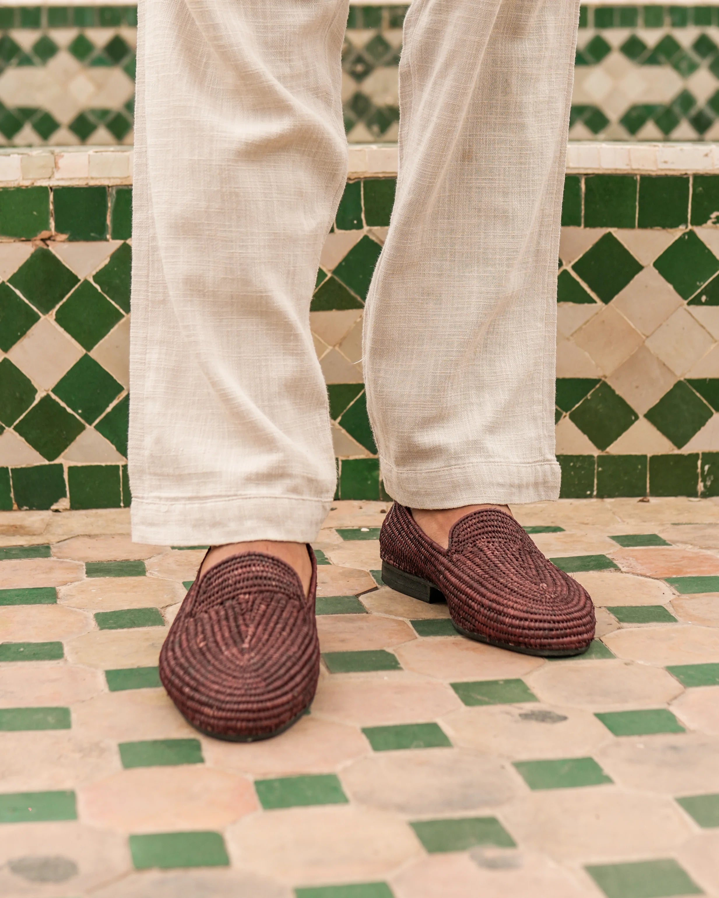 Brown woven shoes worn with light-colored pants on a patterned floor.