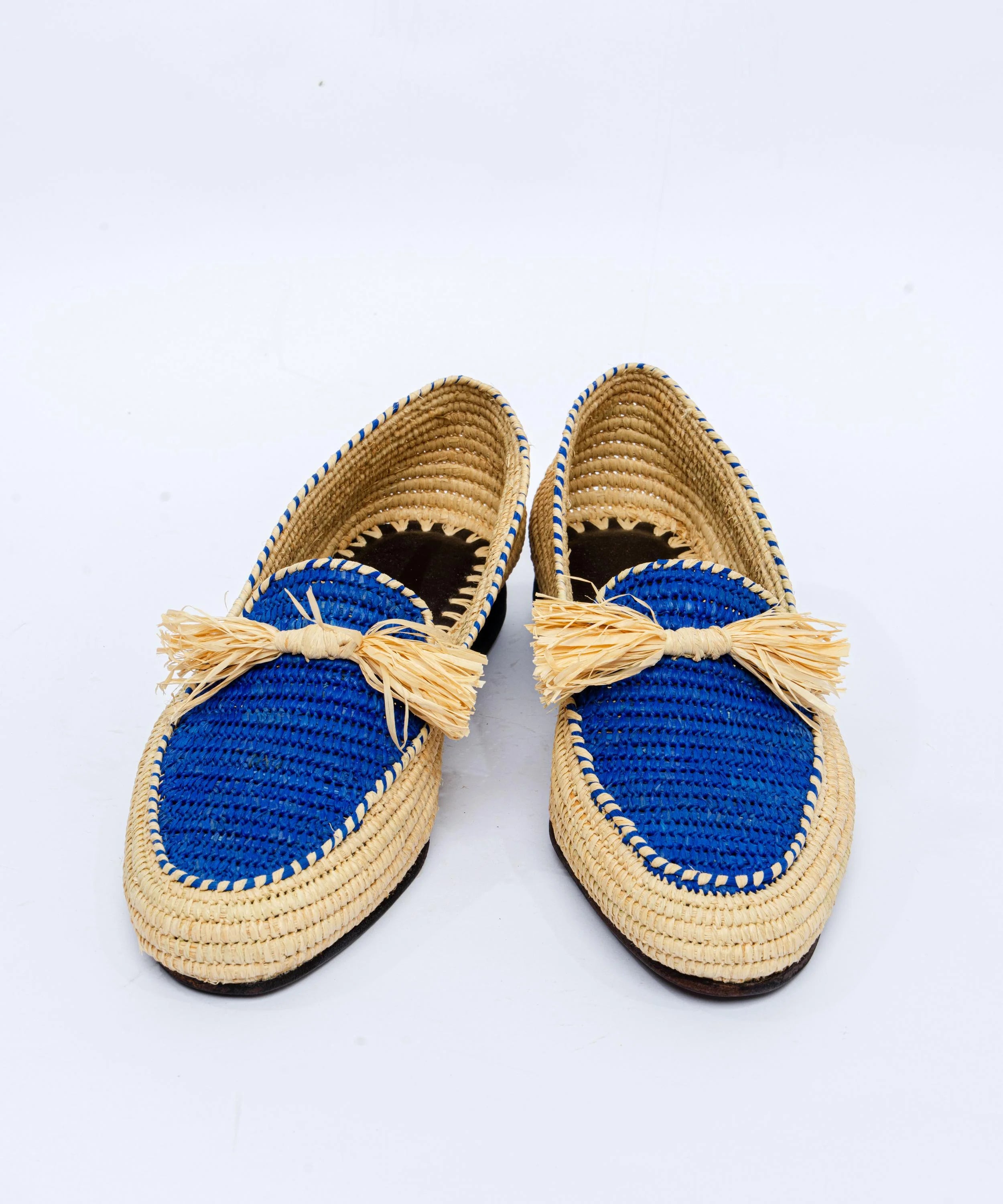 Pair of blue and beige raffia shoes with bow details on a white background