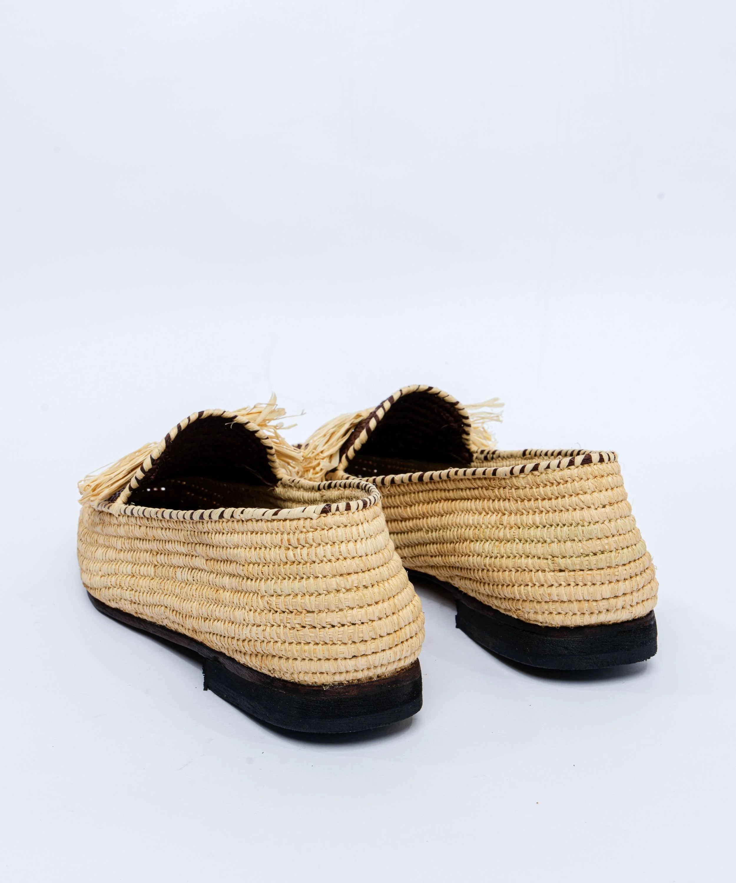 Pair of straw shoes with black soles on a white background