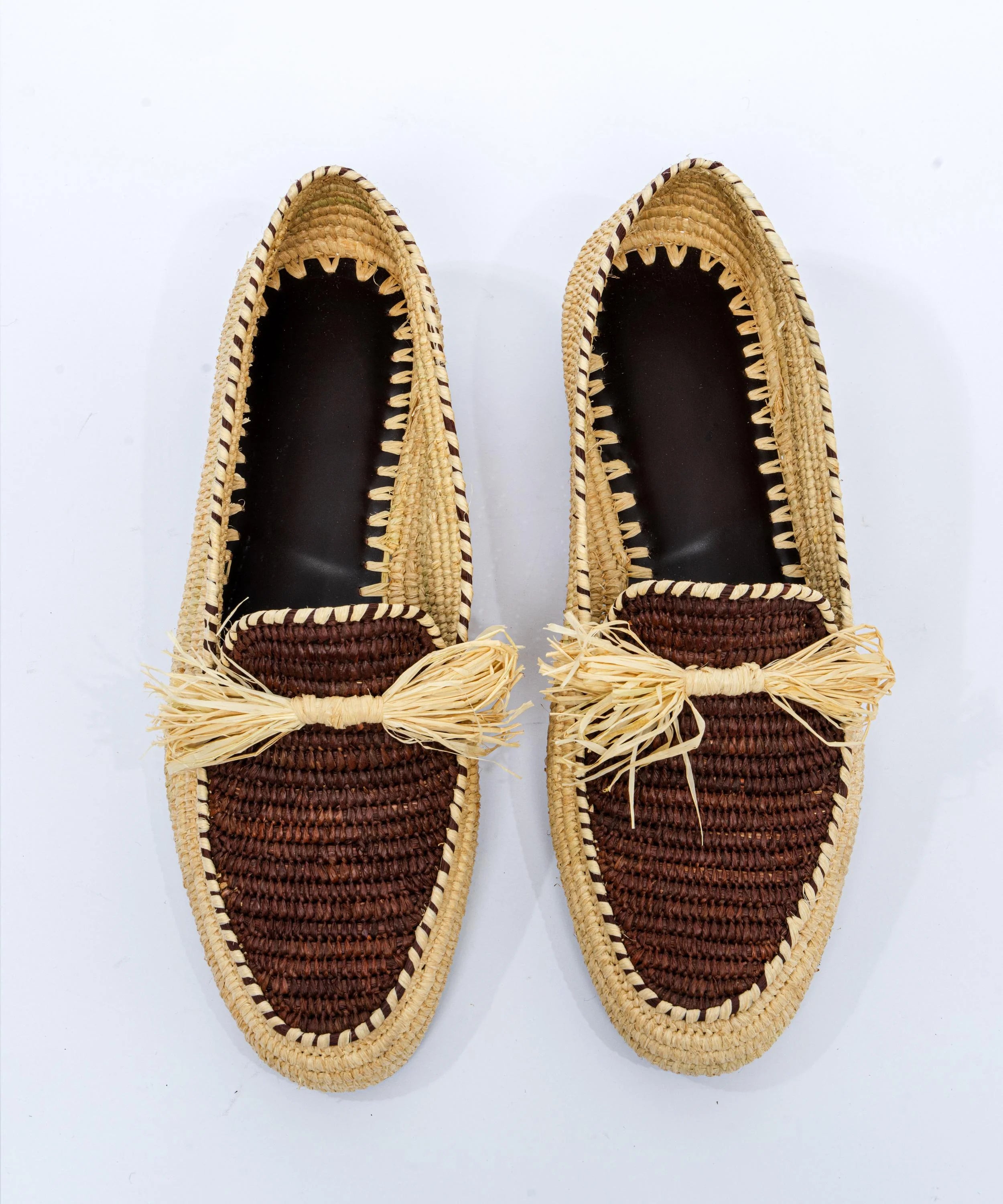 Pair of brown woven shoes with decorative bows on a white background