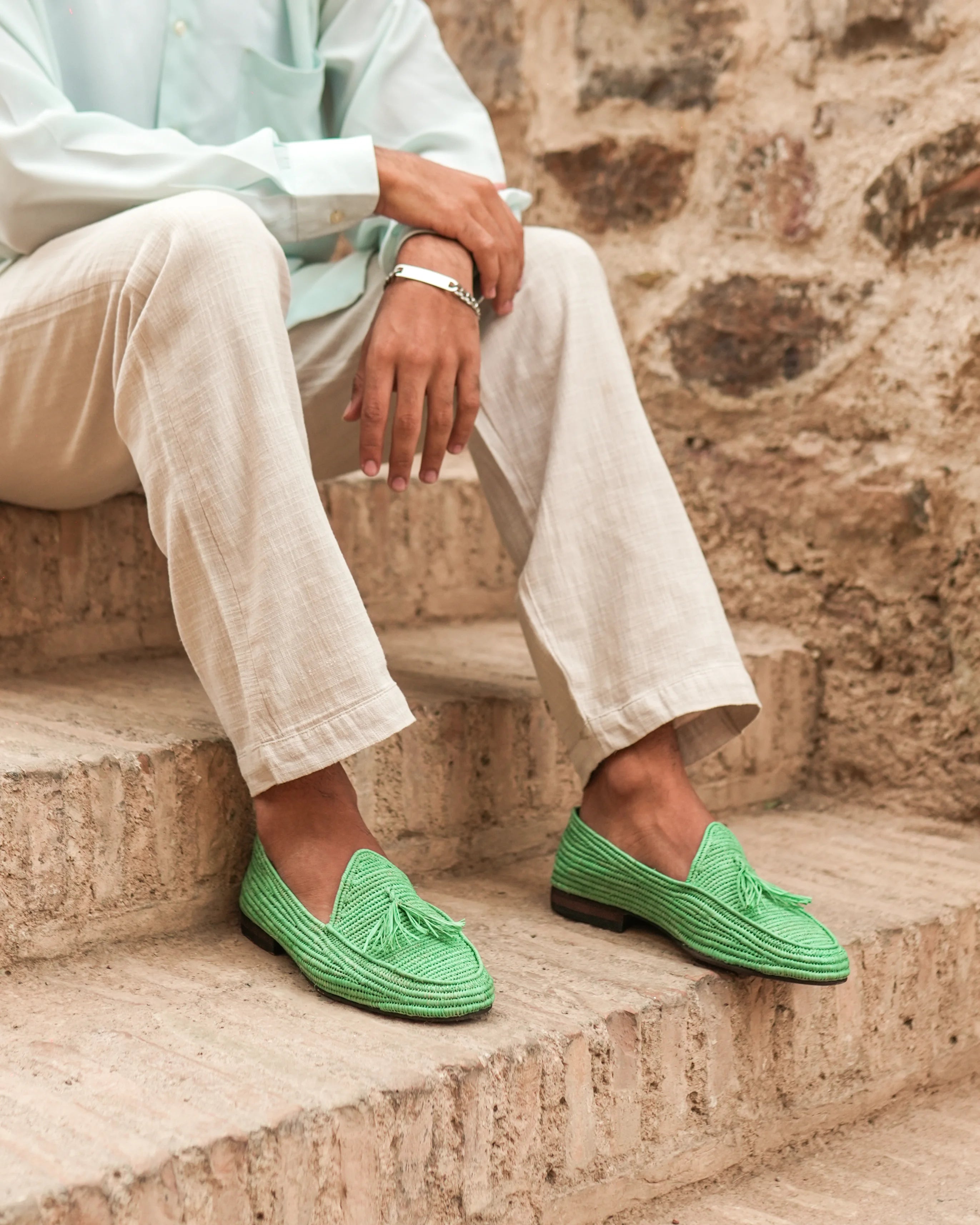 Person wearing green loafers sitting on stone steps with a stone wall background