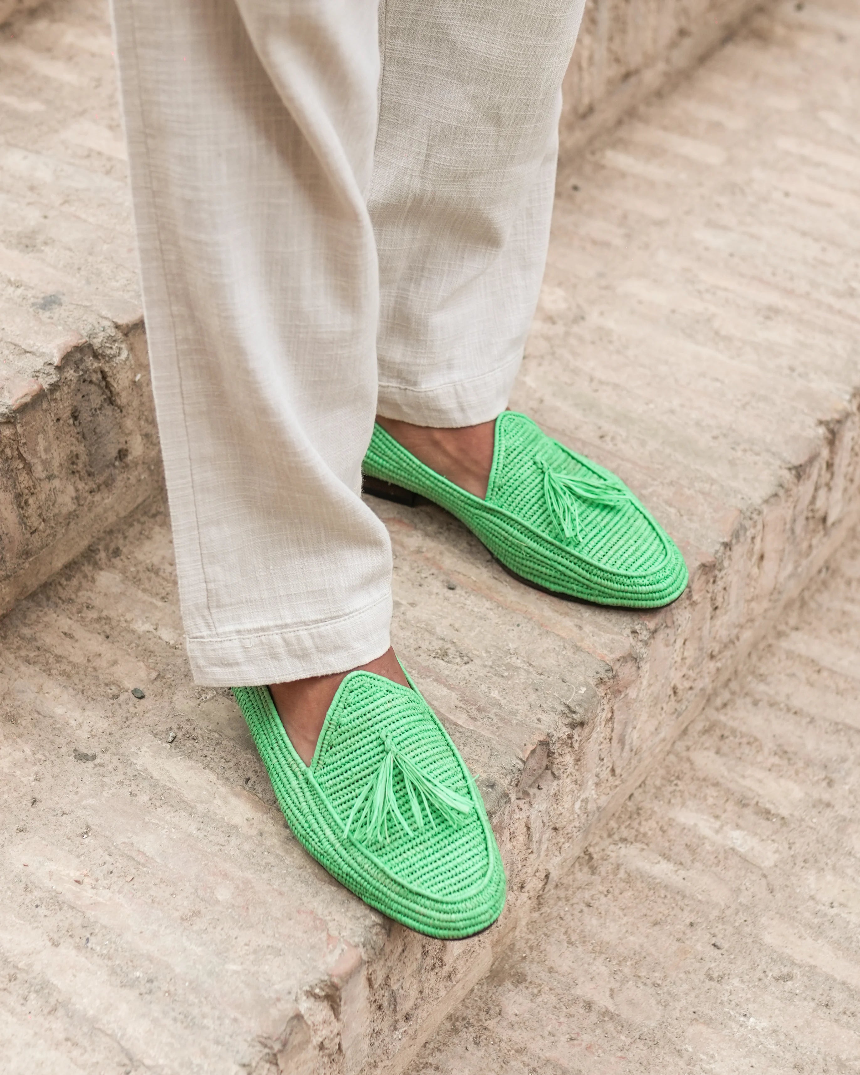 Green slippers worn with light-colored pants on a stone surface