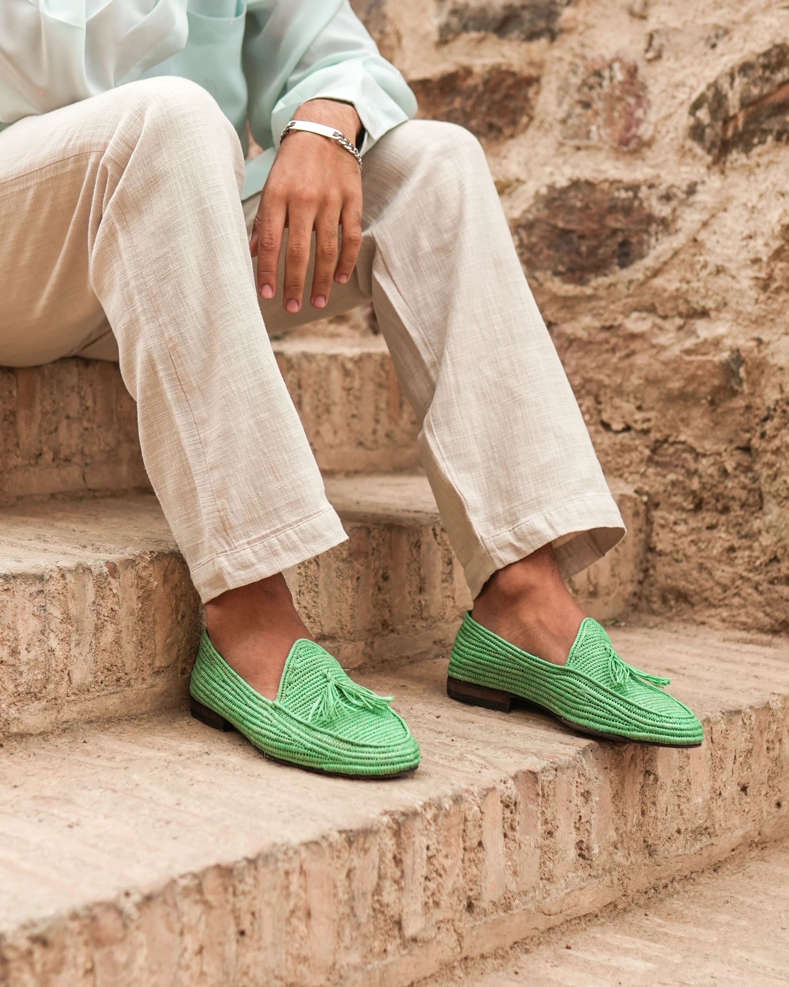 Person wearing green loafers sitting on stone steps with a stone wall background