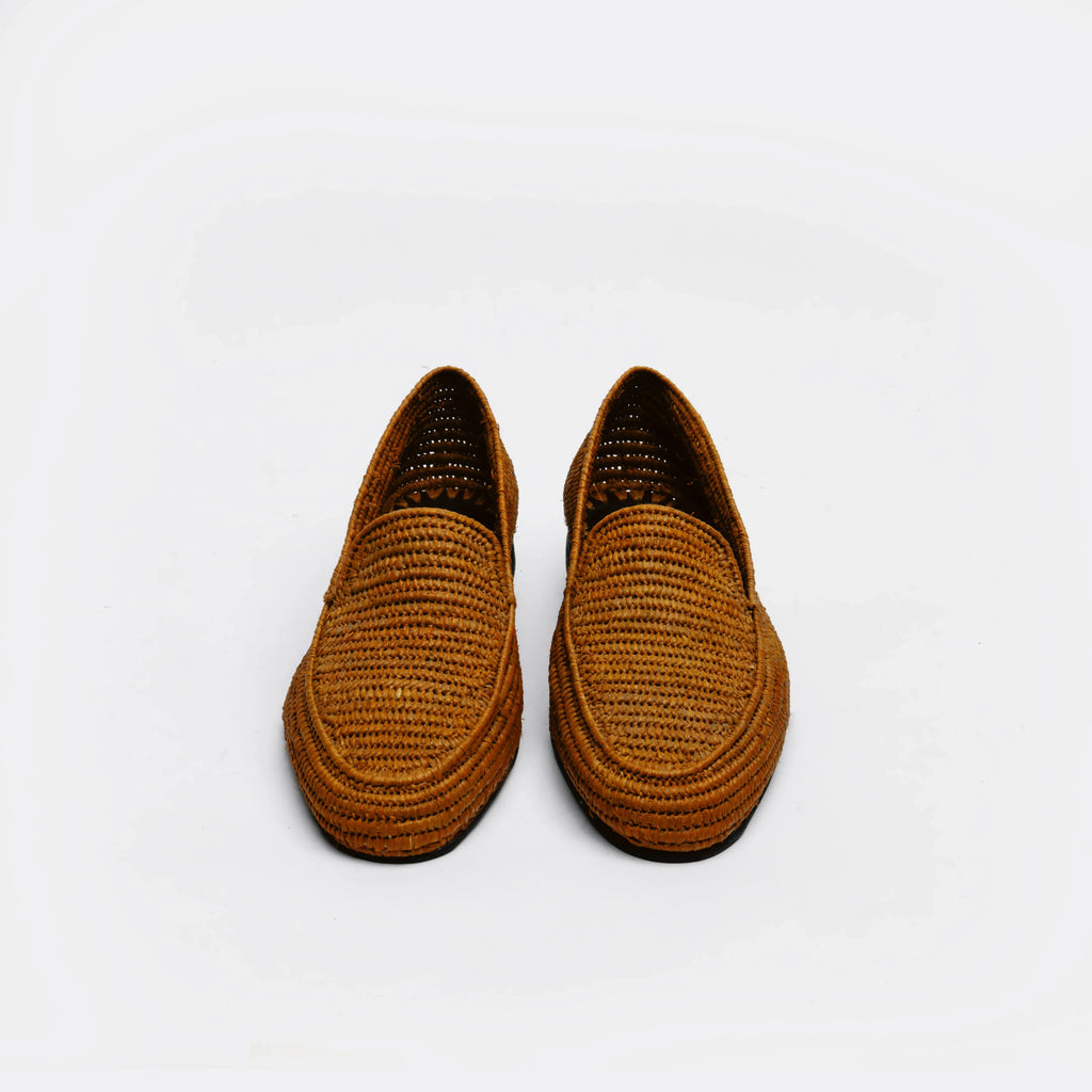 A pair of brown woven slip-on loafers with a braided texture, photographed from a top-down angle on a light gray background.