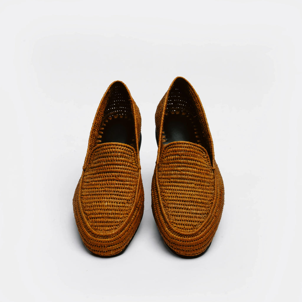 A pair of brown woven slip-on loafers with a textured basketweave pattern, shown from a top-down view on a light gray background.