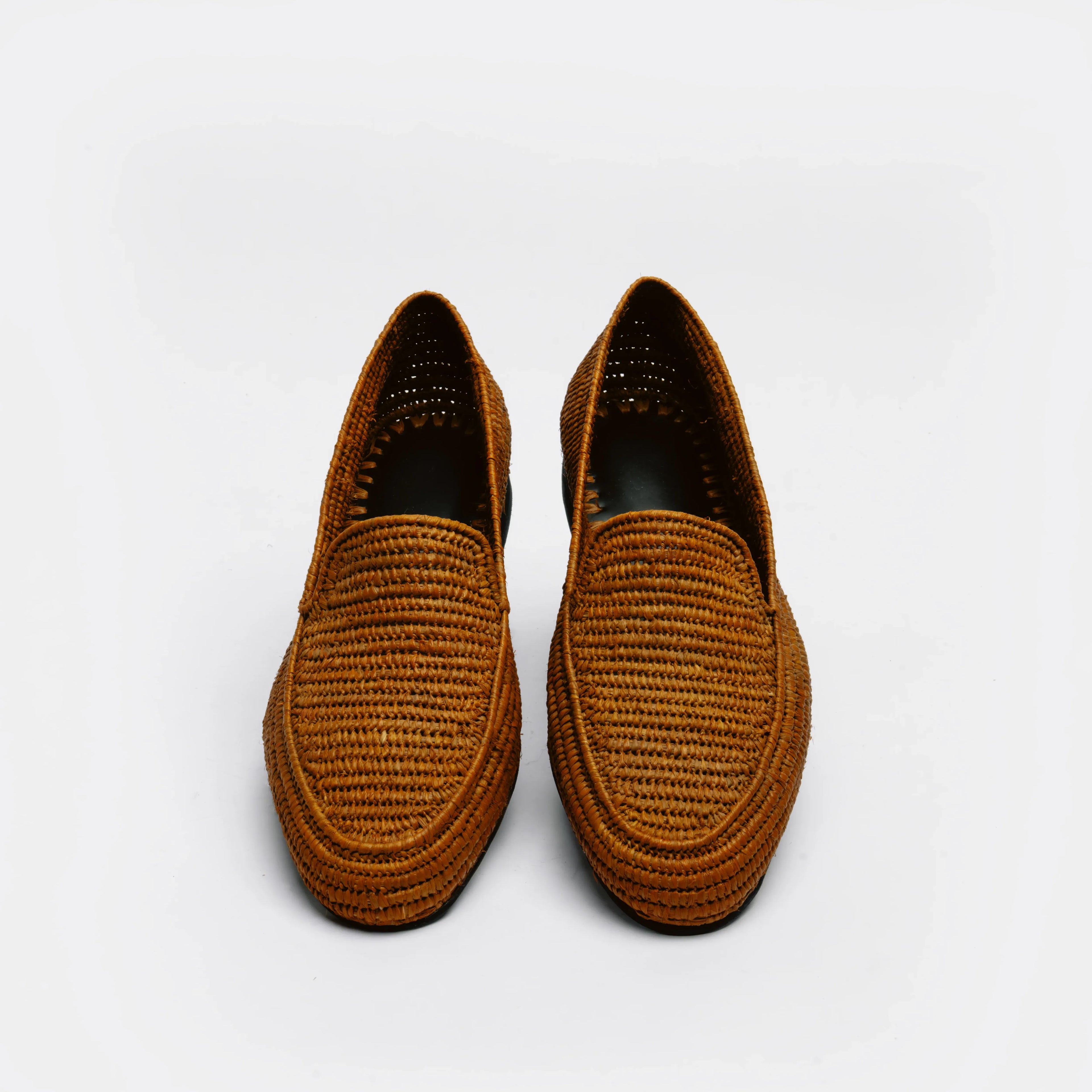 A pair of brown woven slip-on loafers with a textured basketweave pattern, shown from a top-down view on a light gray background.