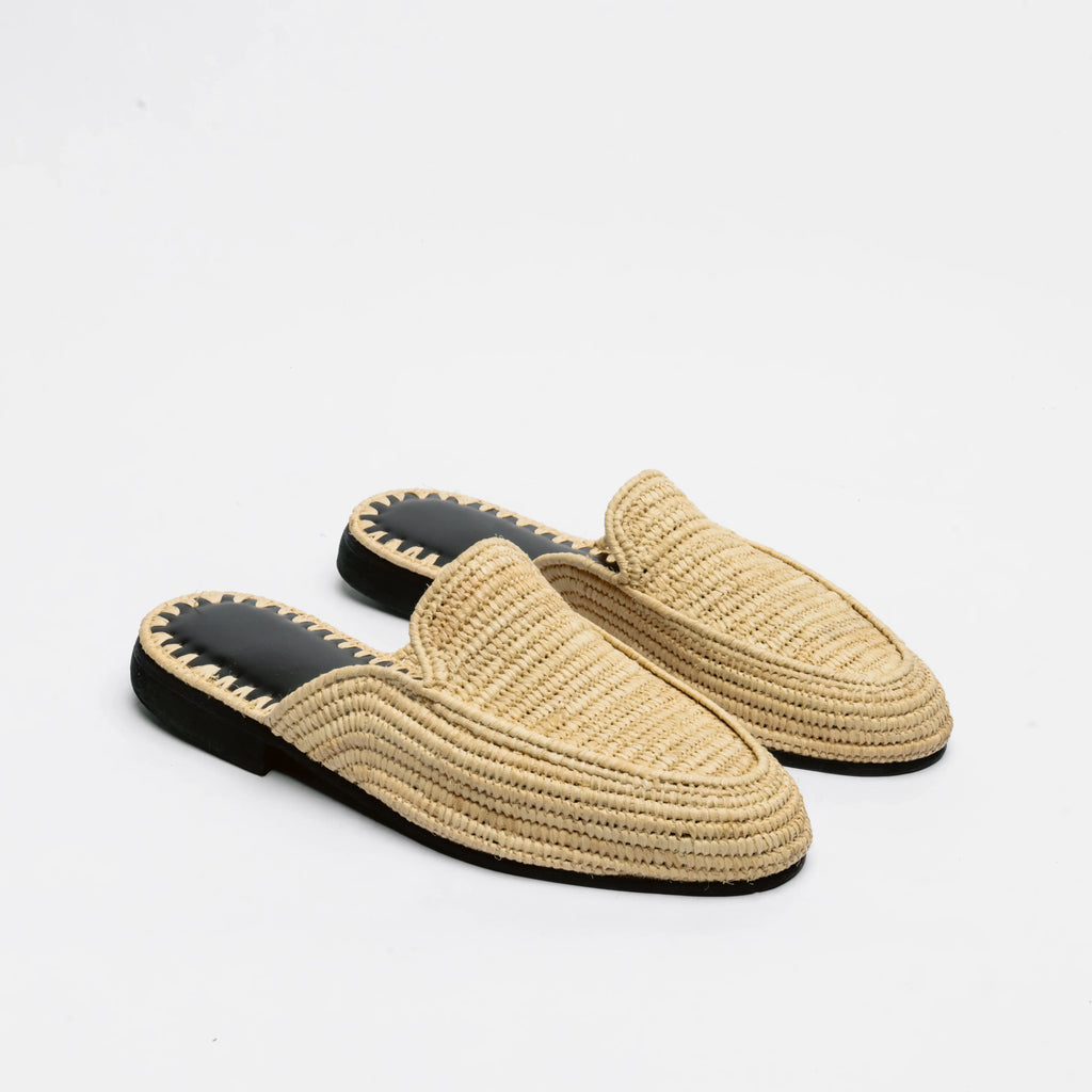 A pair of woven straw slip-on mule loafers with black soles and a decorative zigzag stitch detail around the edge, shown on a plain white background.