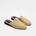 A pair of woven straw slip-on mule loafers with black soles and a decorative zigzag stitch detail around the edge, shown on a plain white background.