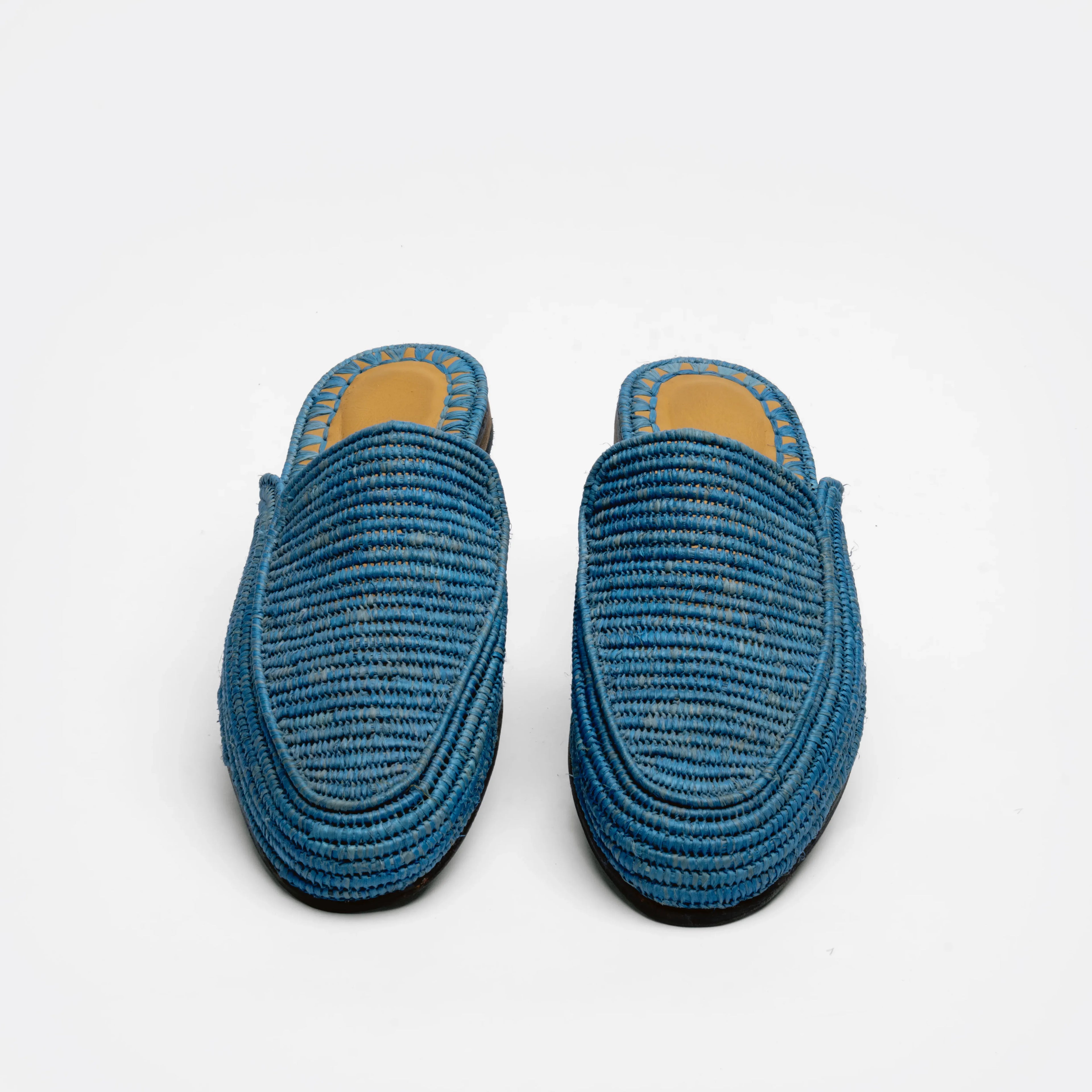 A pair of blue woven raffia mule slippers with a tan insole, shown from a top-down view on a white background.