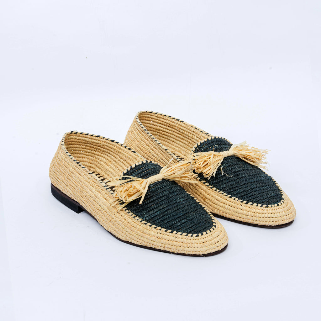 A pair of woven straw loafers with dark green toe caps and tassels, shown on a clean white background.
