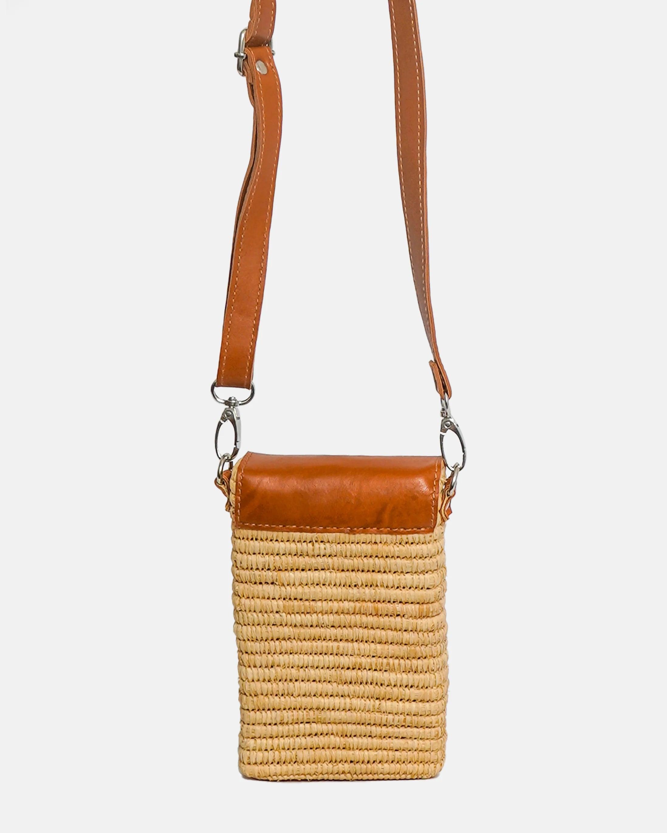 Crossbody bag with straw body and brown leather strap on a white background