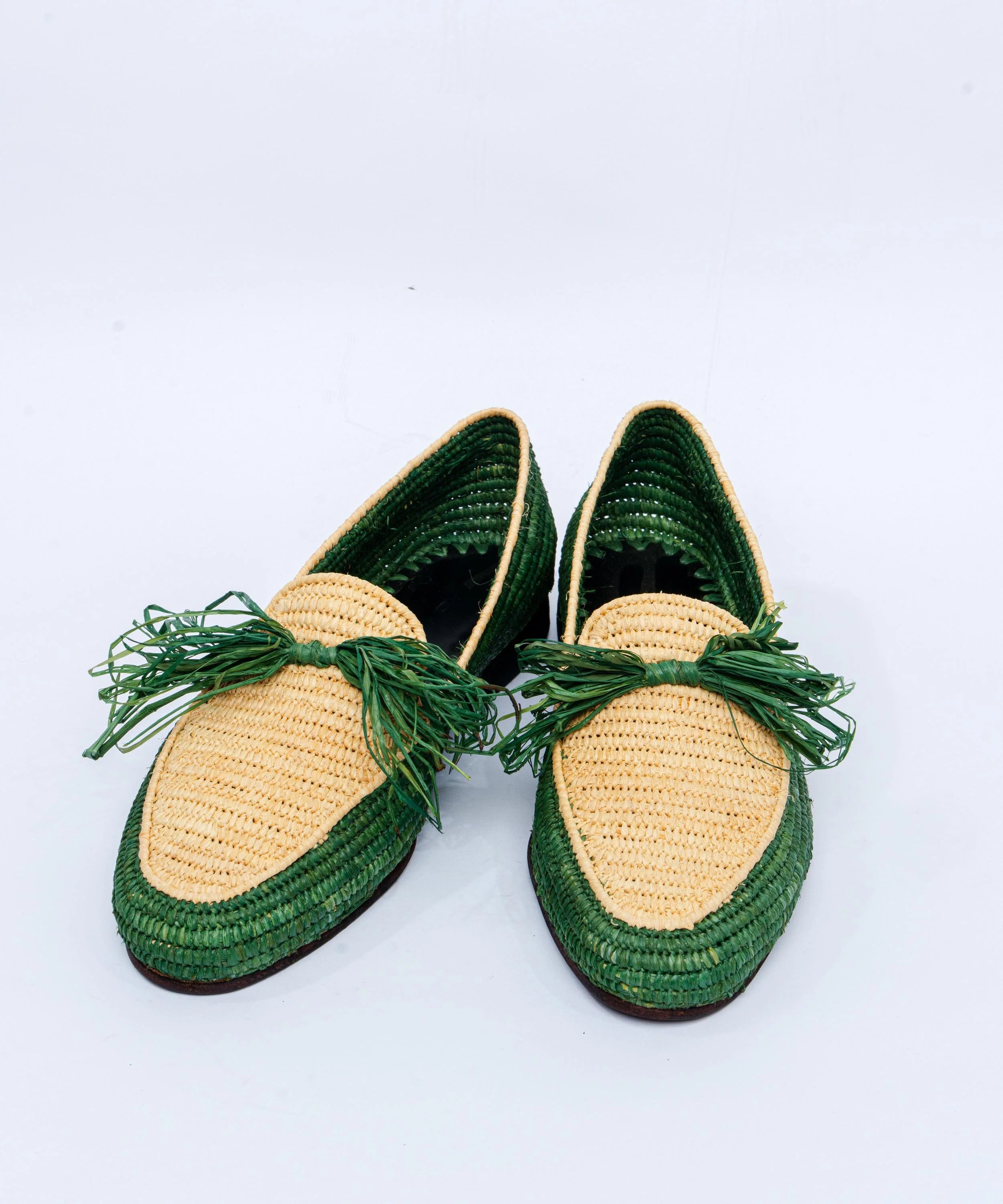 Pair of straw shoes with green accents on a white background