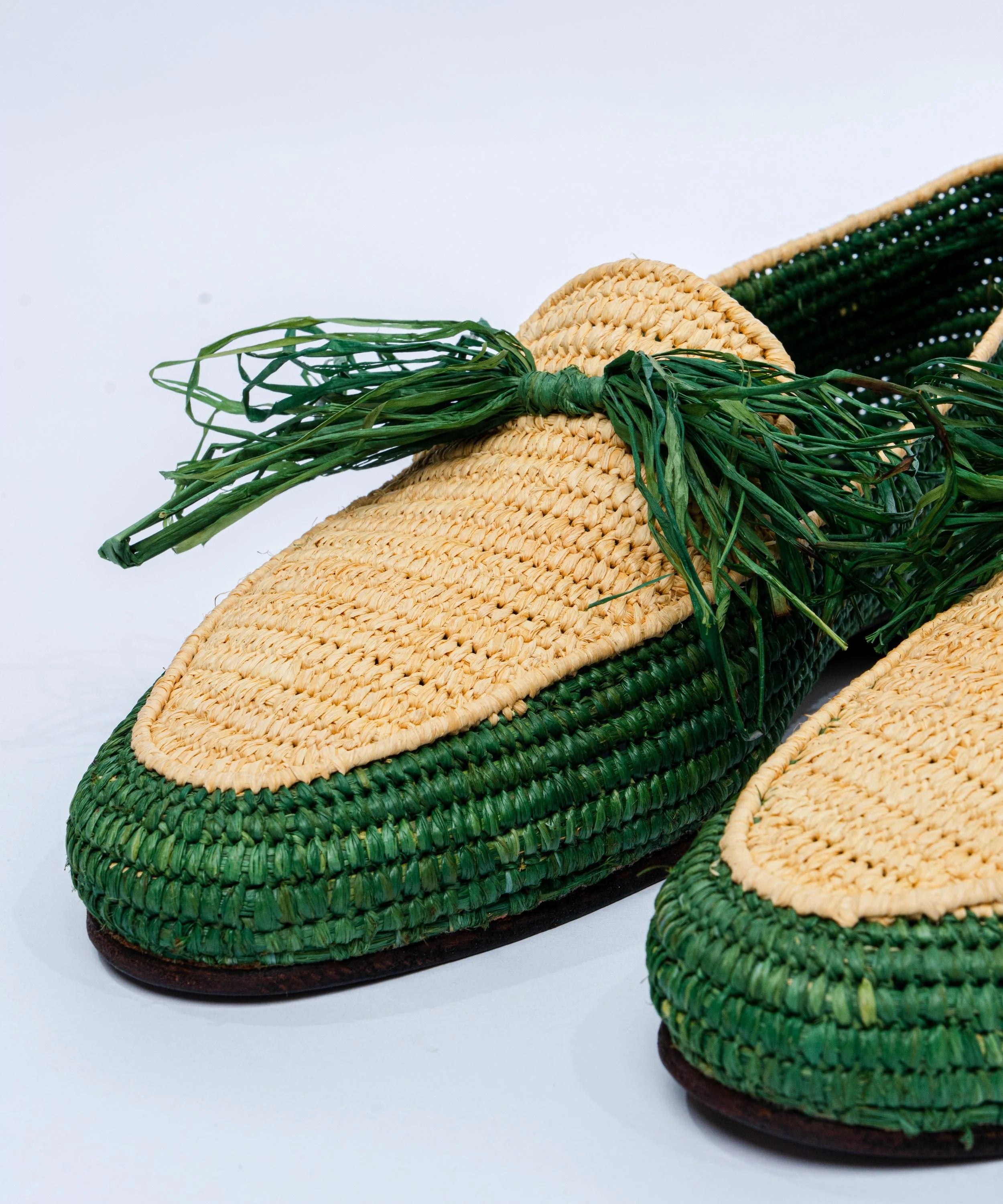 Green and beige woven shoes with grass-like decoration on a light gray background