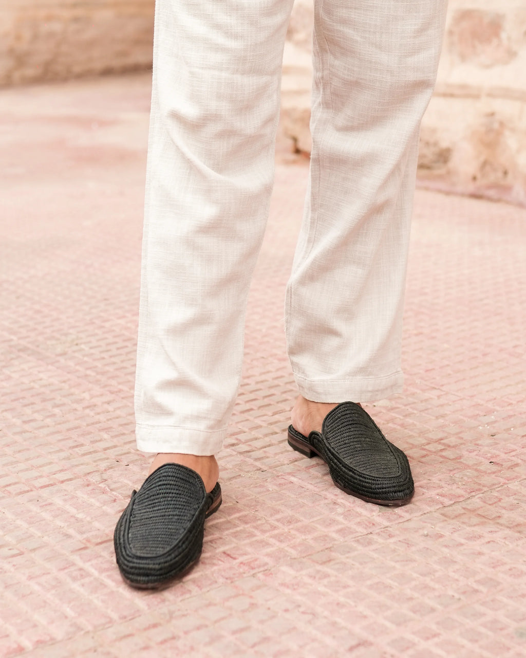 Person wearing black slip-on shoes and white pants on a textured pink surface