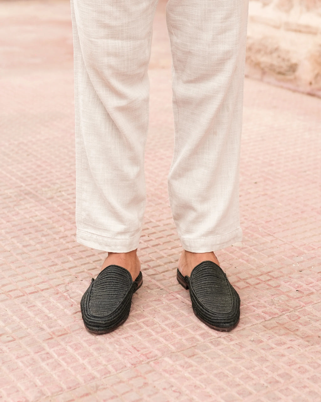 Person wearing white pants and black slip-on shoes on a pink textured surface