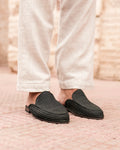 Person wearing black slippers on a pink textured surface
