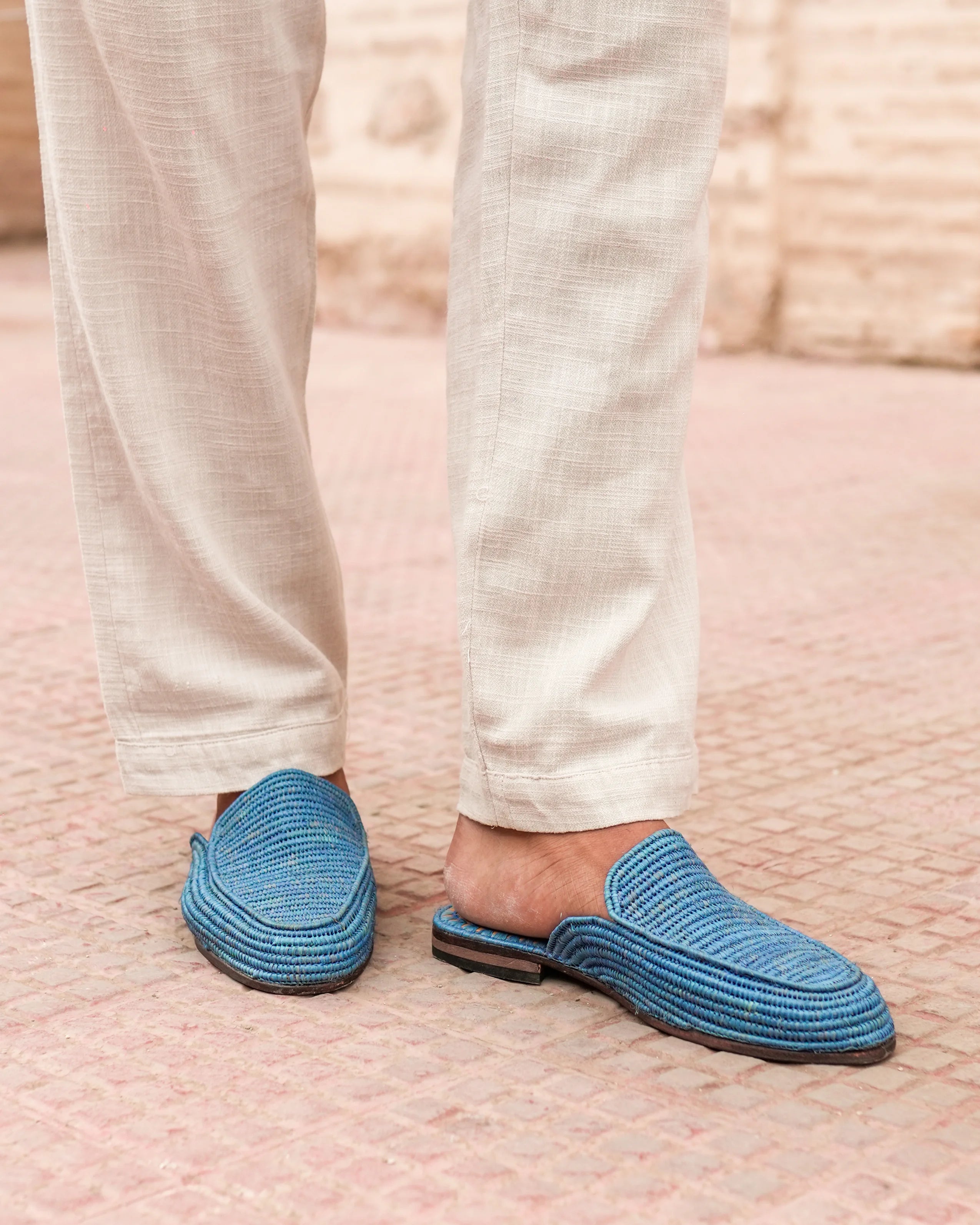 Blue slippers worn with light-colored pants on a textured surface