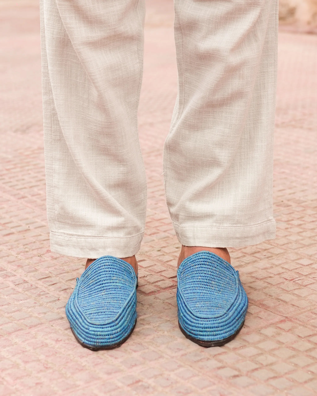Blue slippers worn with white pants on a textured pink surface