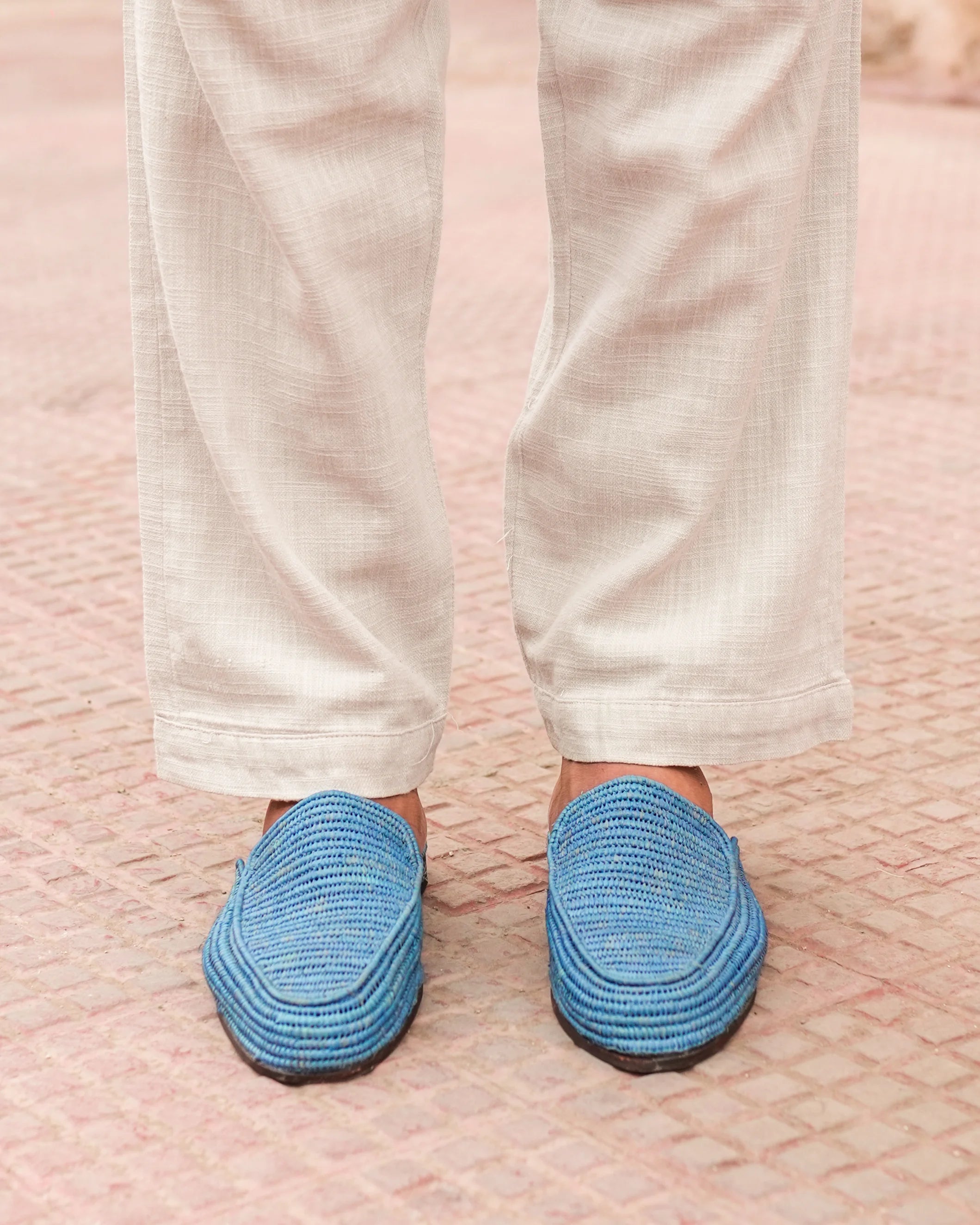 Blue slippers worn with white pants on a textured pink surface