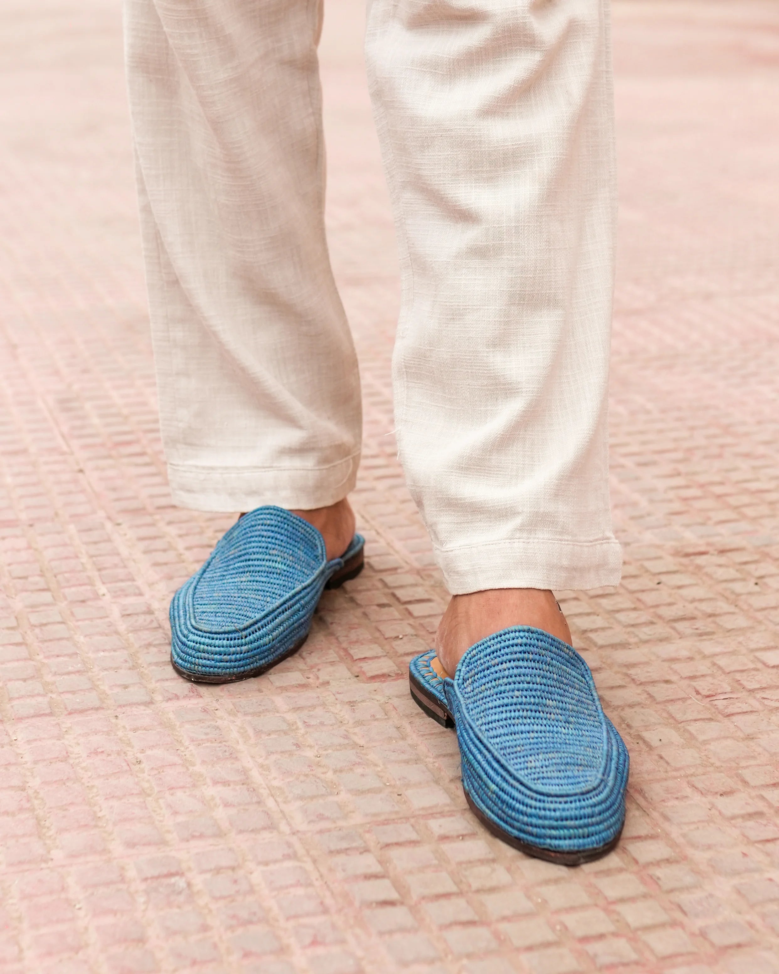 Blue slippers worn with white pants on a textured surface