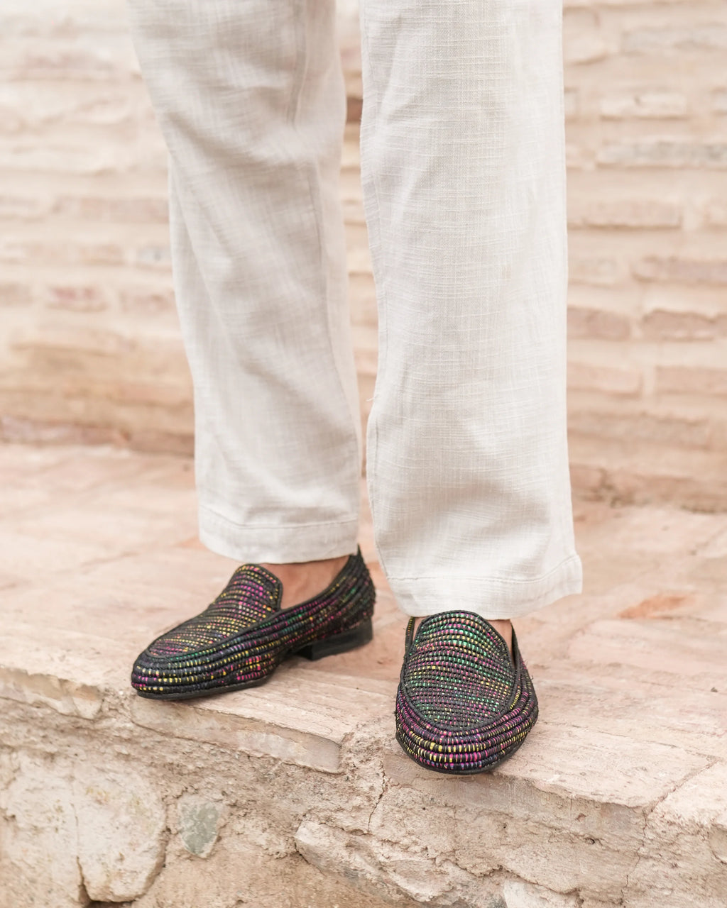 Multicolored loafers worn with white pants on a stone surface