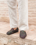 Multicolored loafers worn with white pants on a stone surface