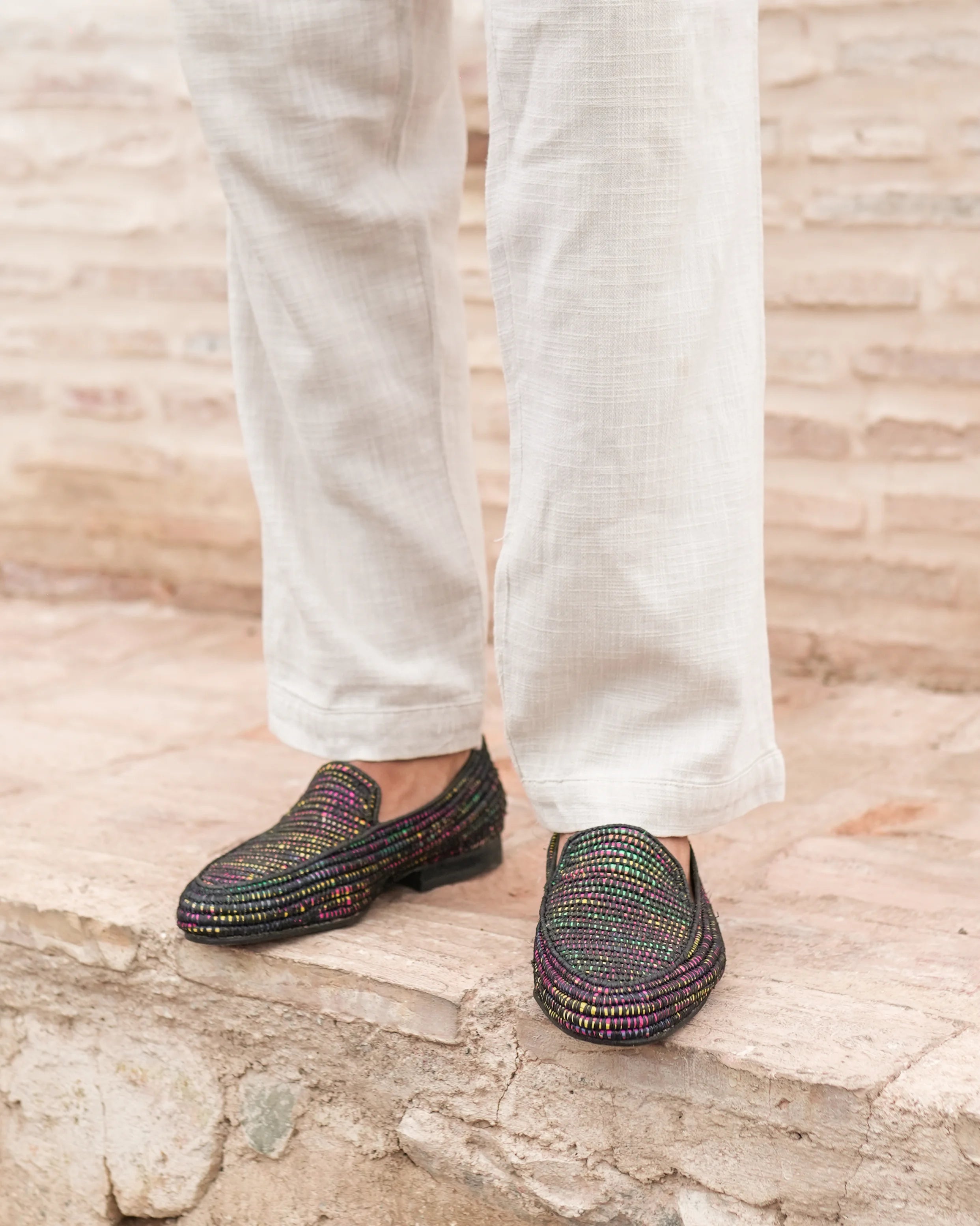 Multicolored loafers worn with white pants on a stone surface
