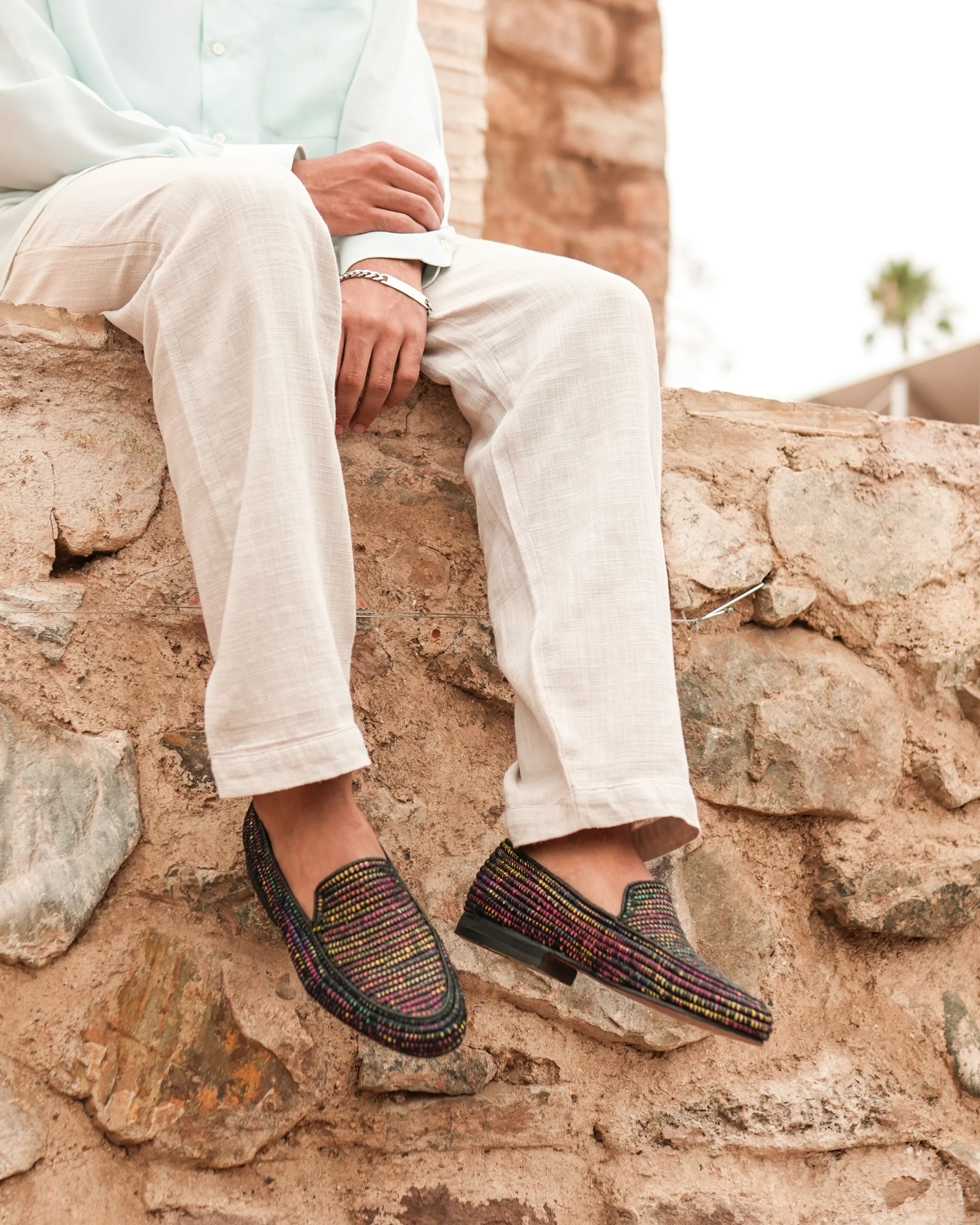 Person wearing patterned loafers sitting on a stone wall.