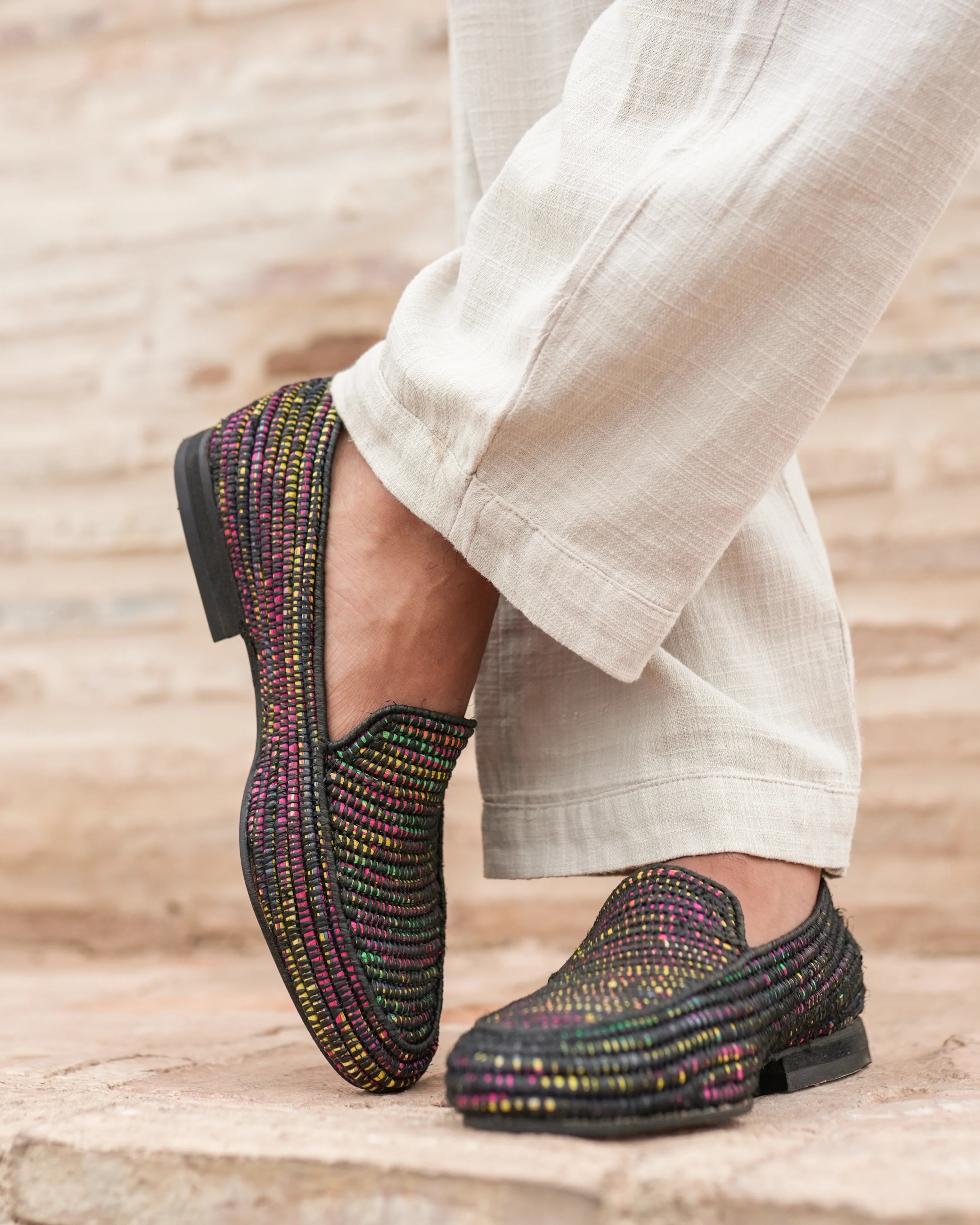 Black woven shoes worn with light-colored pants on a wooden floor.
