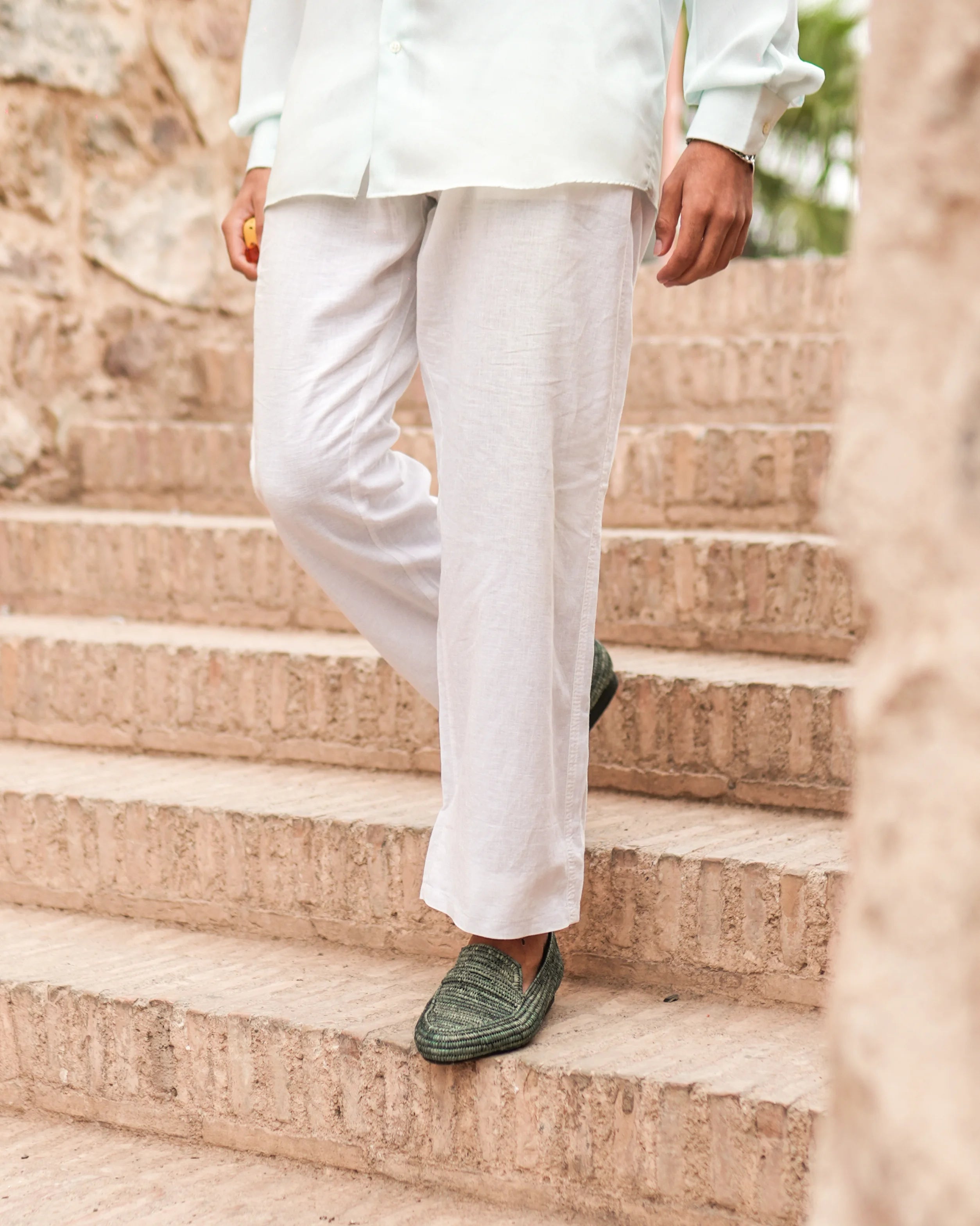 Person wearing white pants and green raffia shoes walking up stone steps.